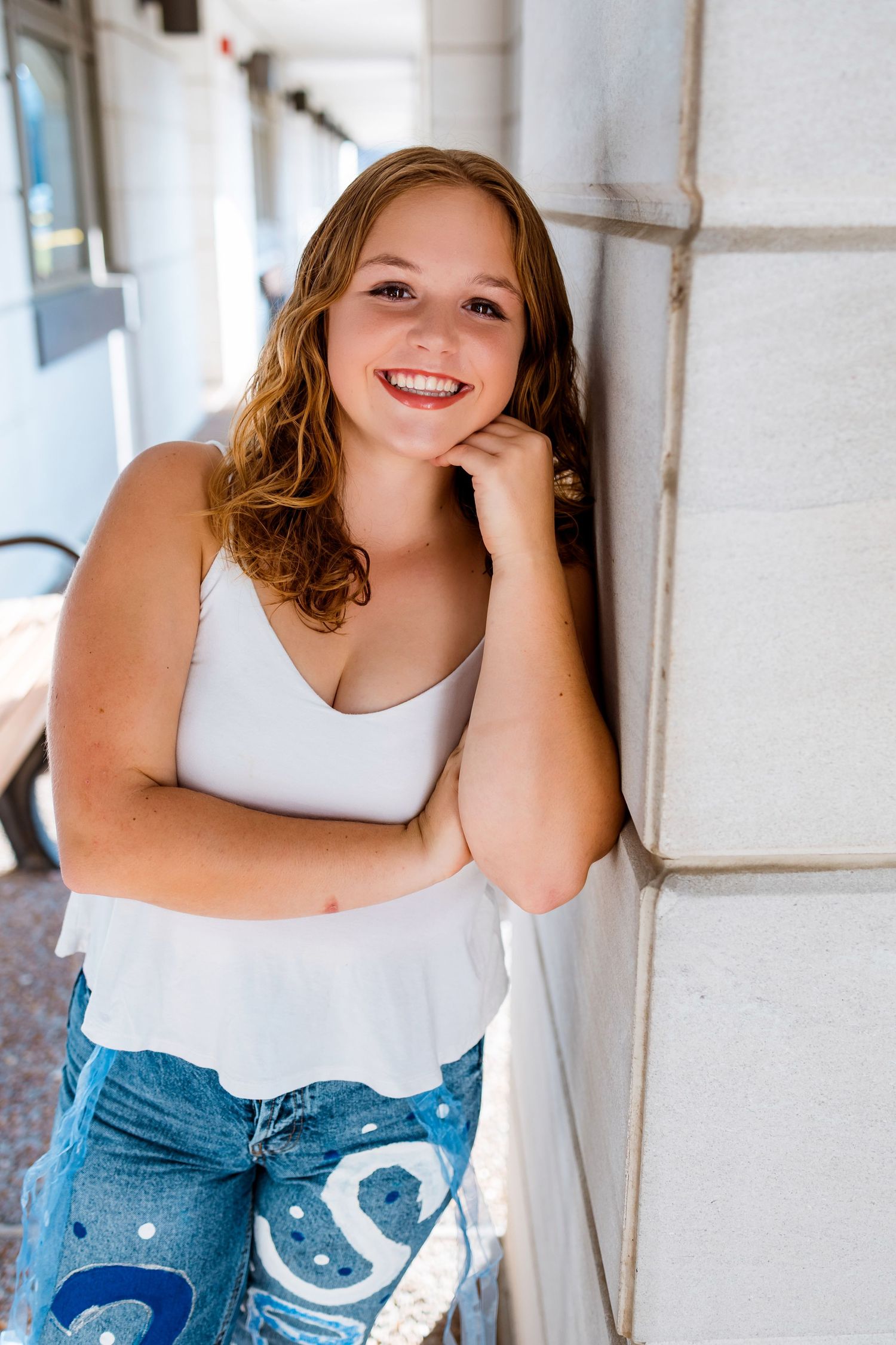 A person in a white tank top and jeans poses against a white wall in a casual portrait series.