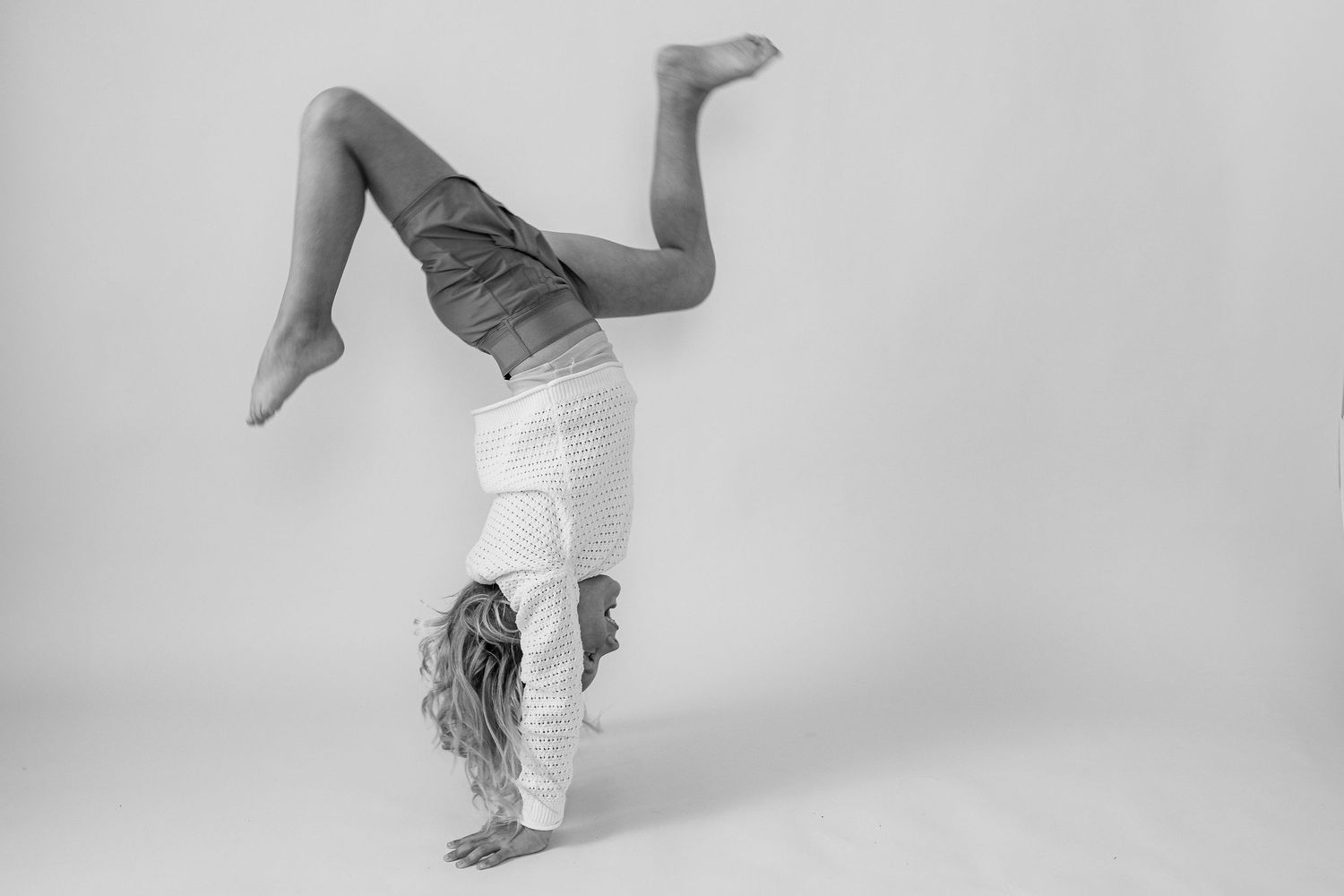 A dancer performs a handstand against a stark white background, showing graceful form in black and white photography.