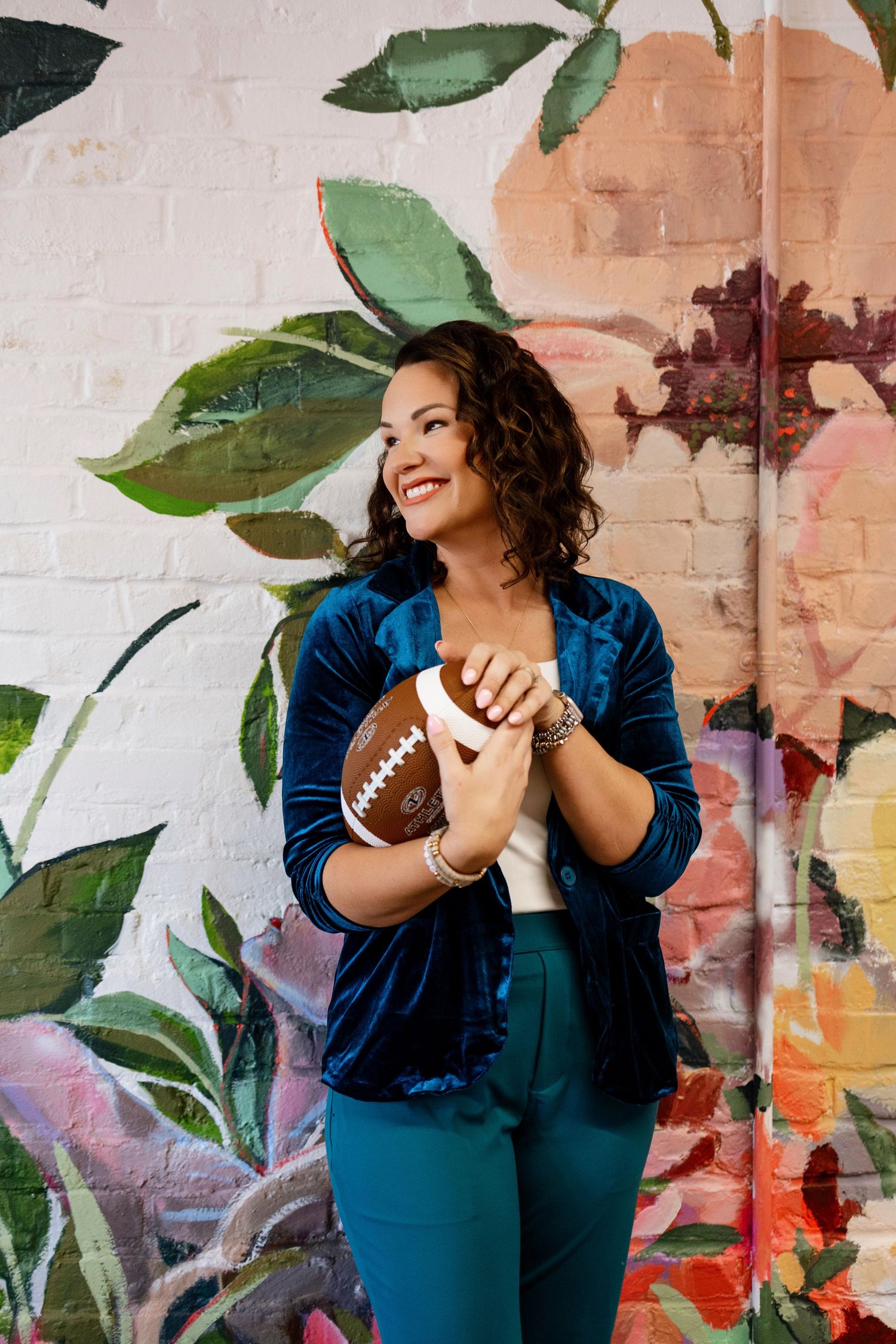 Playful brand photoshoot with football prop against floral painted wall backdrop.