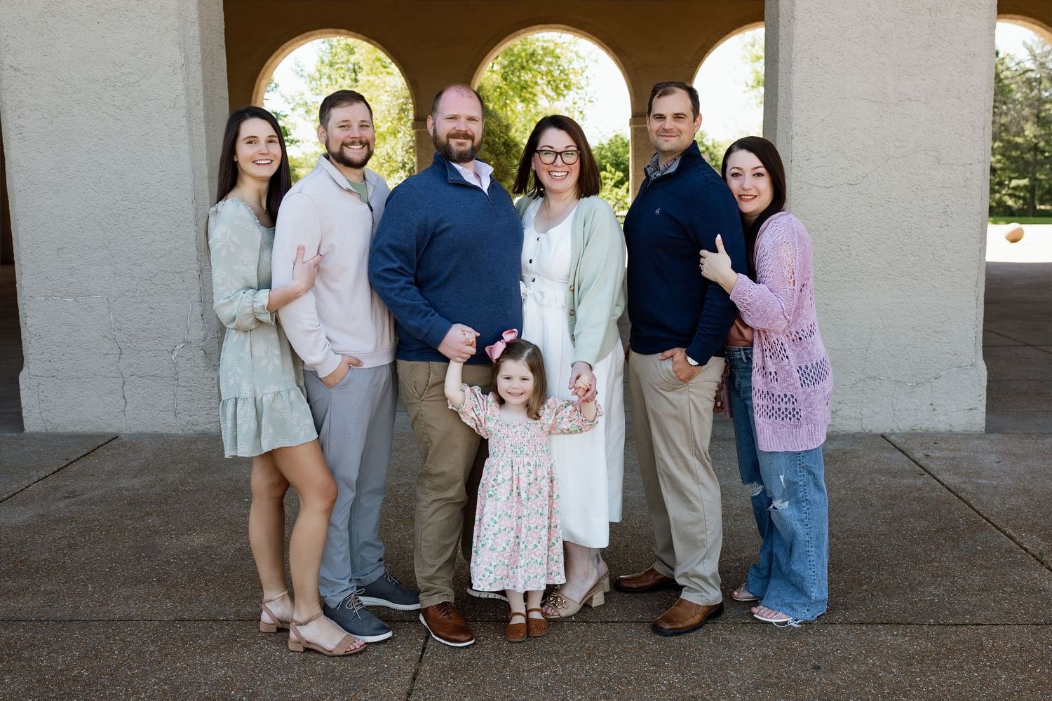 Extended family of seven posing together beneath stone arches during an outdoor Metro East photography session