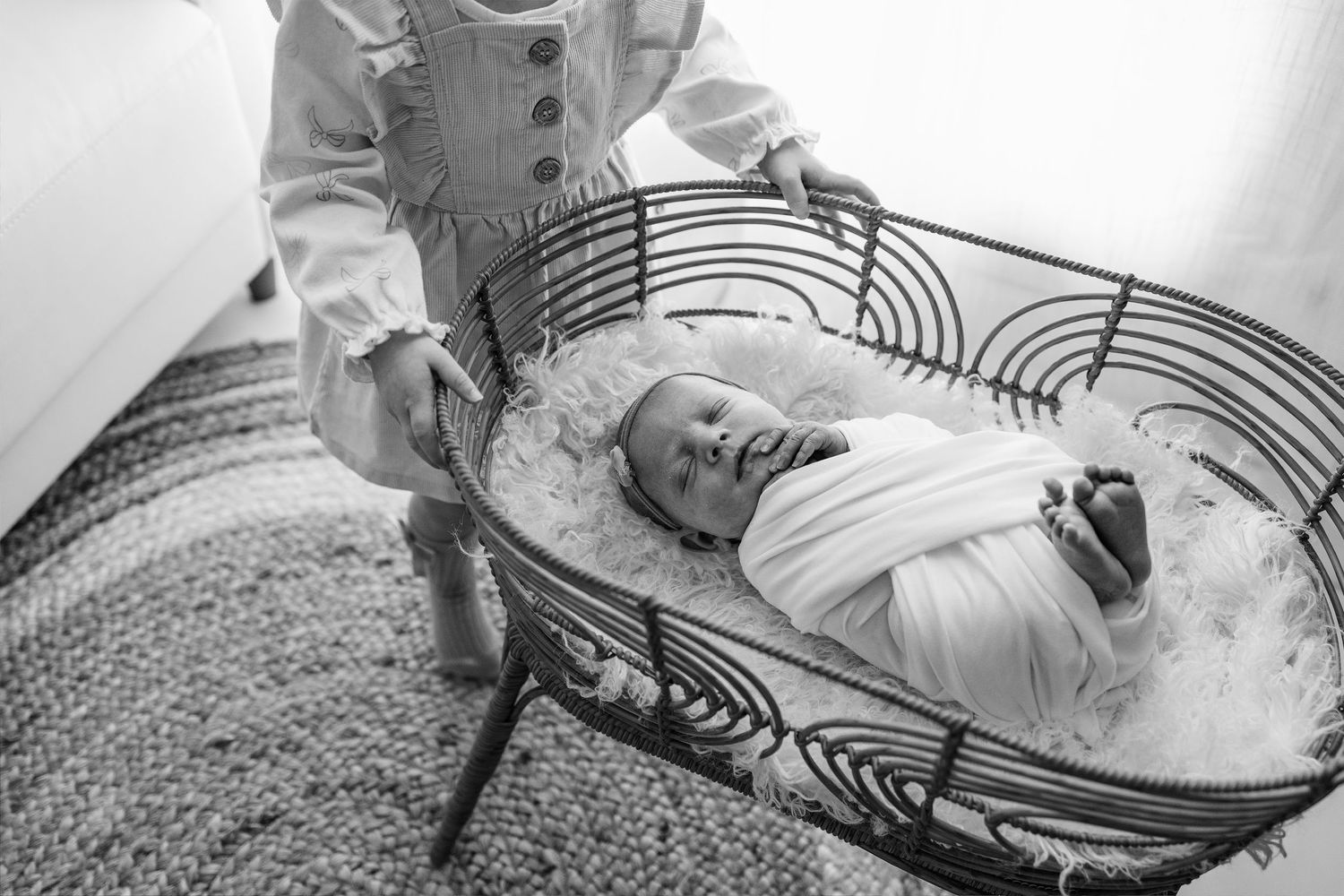 Black and white image of baby resting in decorative bassinet with curved metal design.