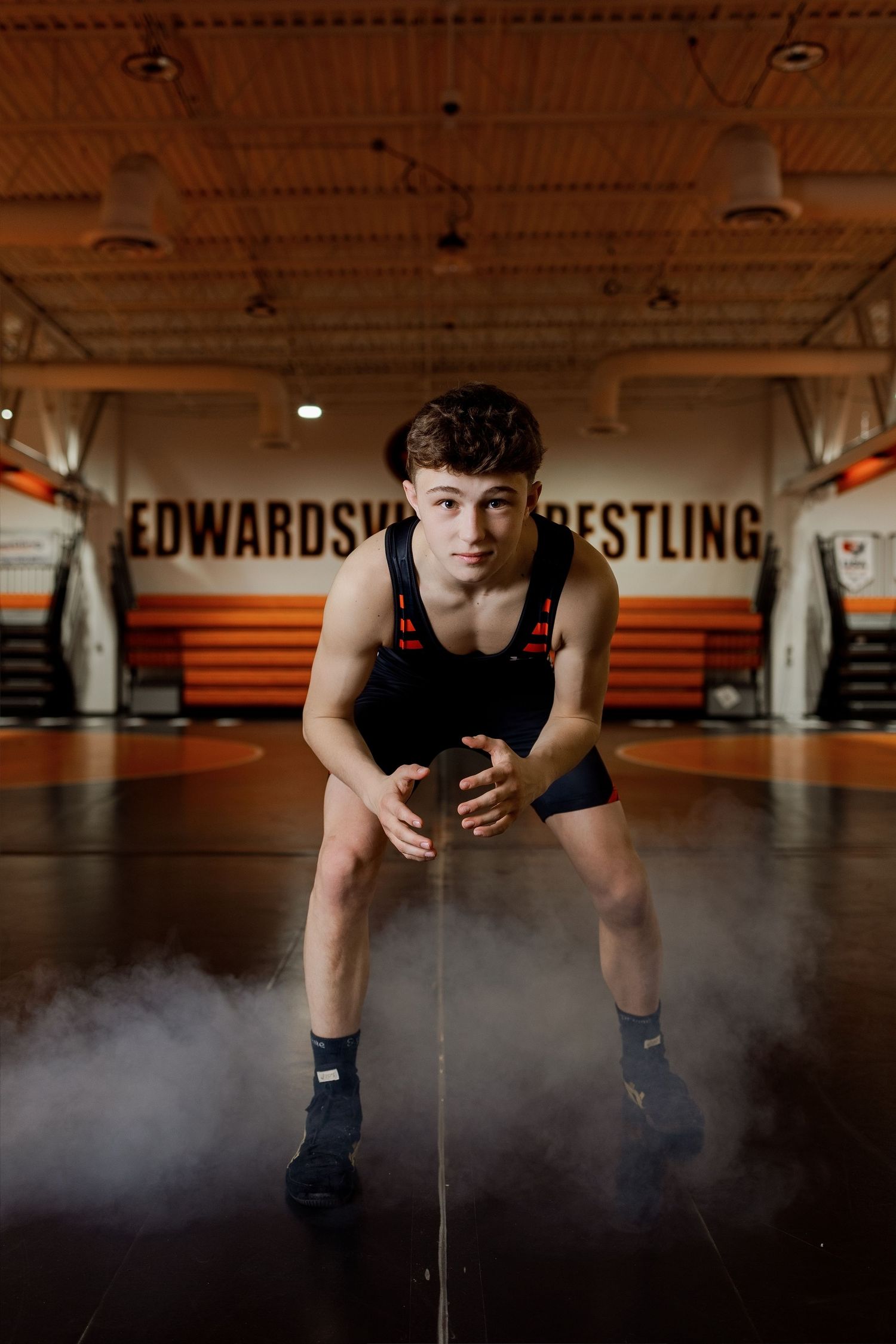 Dramatic low-angle shot of a wrestler in a dark gym with fog effects creating an atmospheric sports portrait.