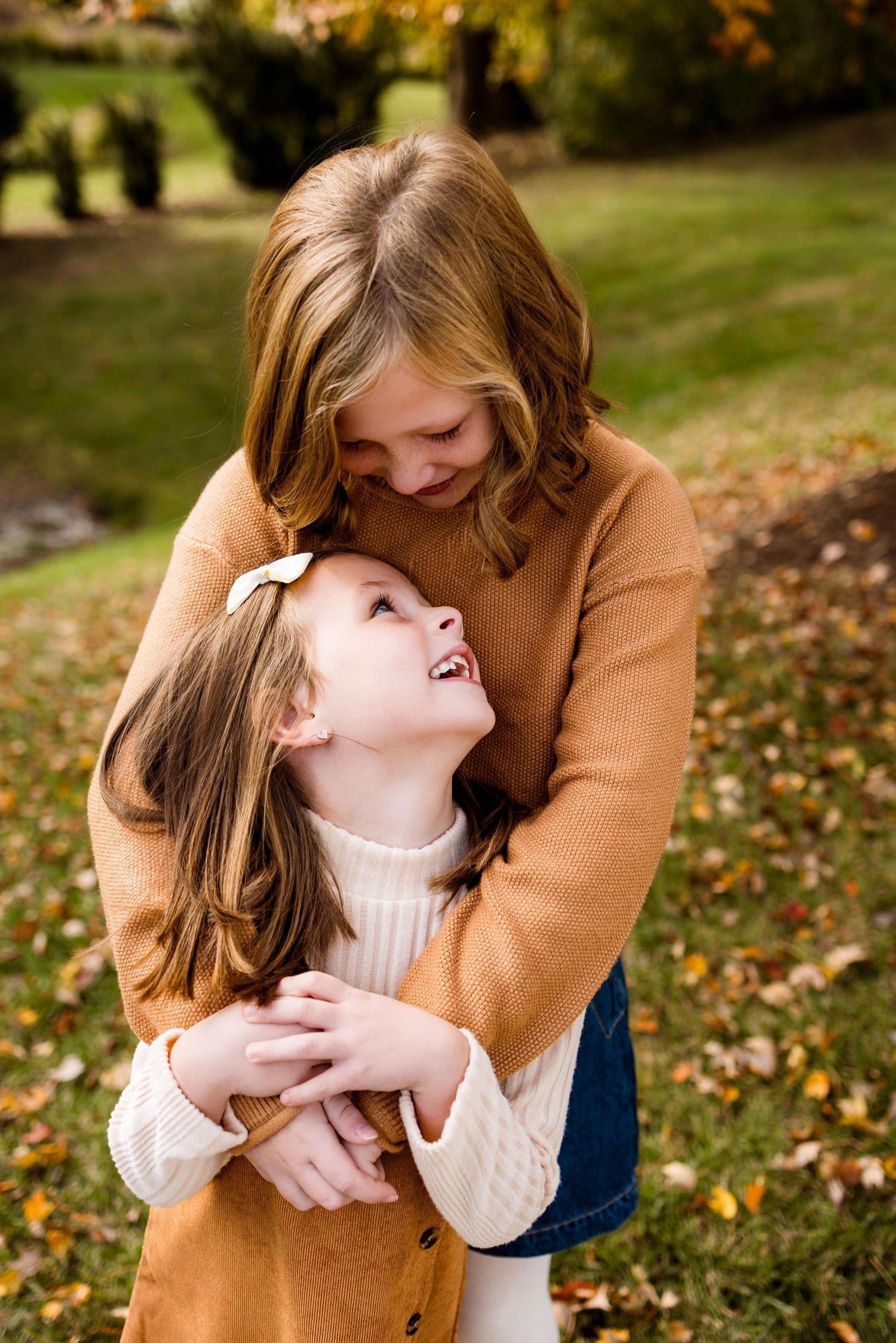 A heartwarming autumn scene shows a tender embrace between parent and child on grass covered with fallen leaves.