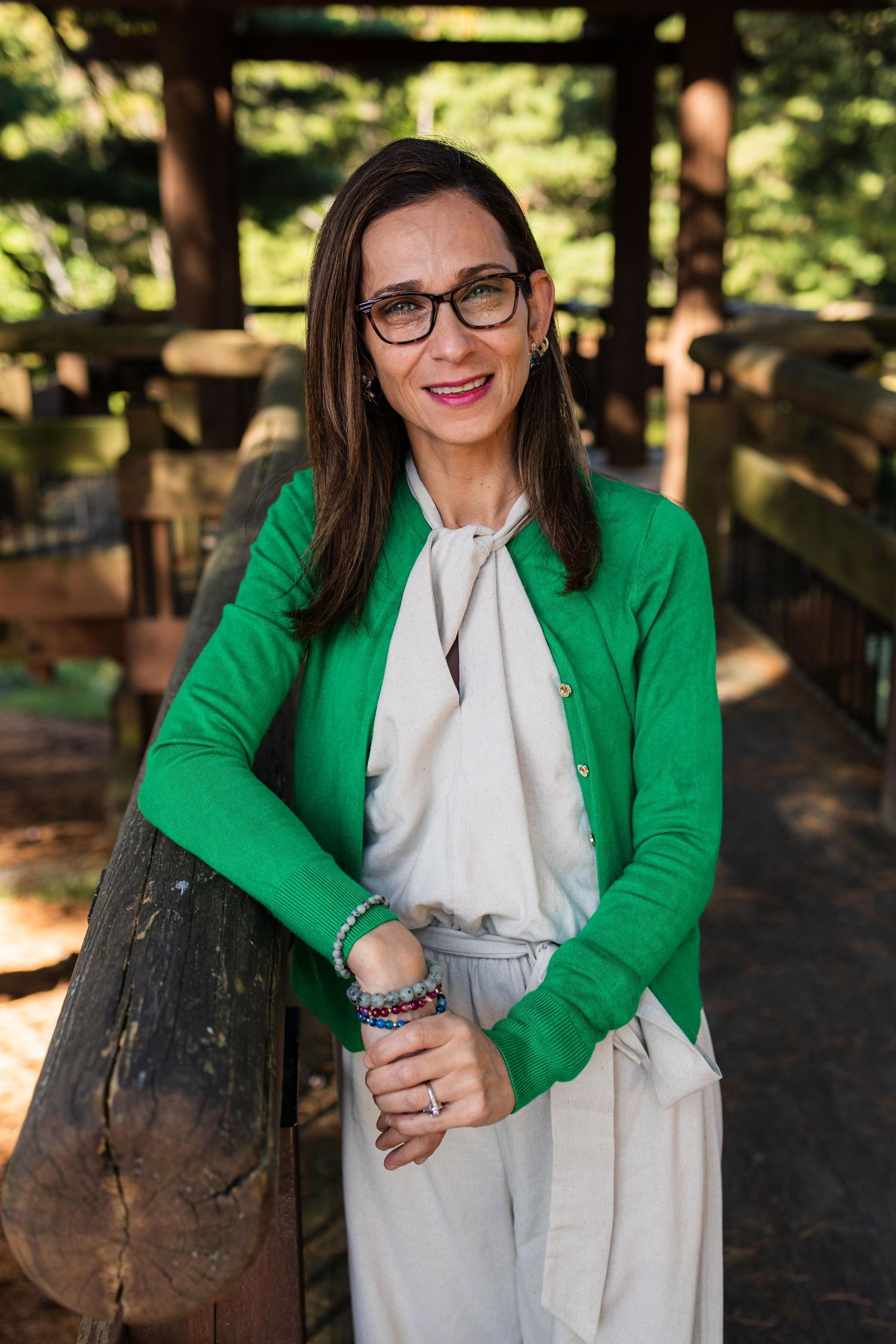 A person in a bright green cardigan and white dress sits on a wooden bench in a sunlit outdoor setting.