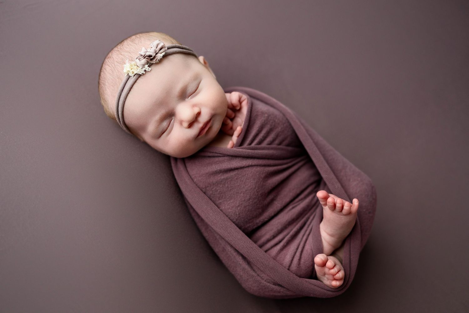 A series of seven connected photos showing a swaddled newborn baby in brown fabric against a dark background.