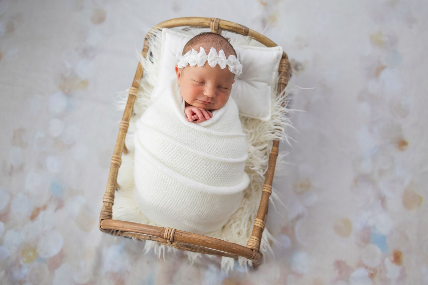 Newborn baby peacefully sleeping while swaddled in white fabric inside a small rustic wooden basket.