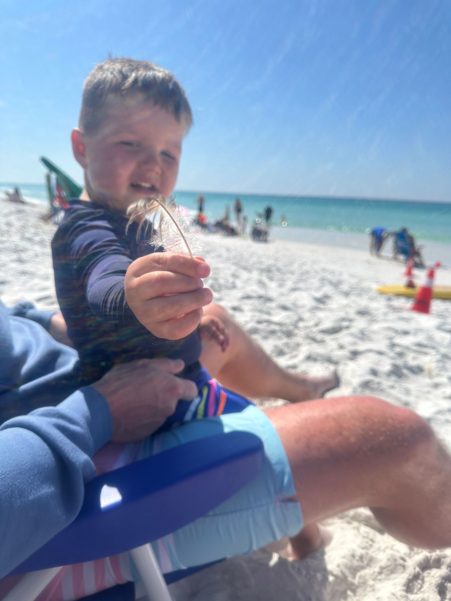 Close-up of child holding small beach discovery while sitting on blue beach chair.