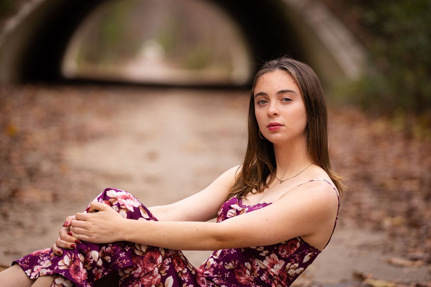 Autumn portrait near stone tunnel featuring floral dress and natural pose.