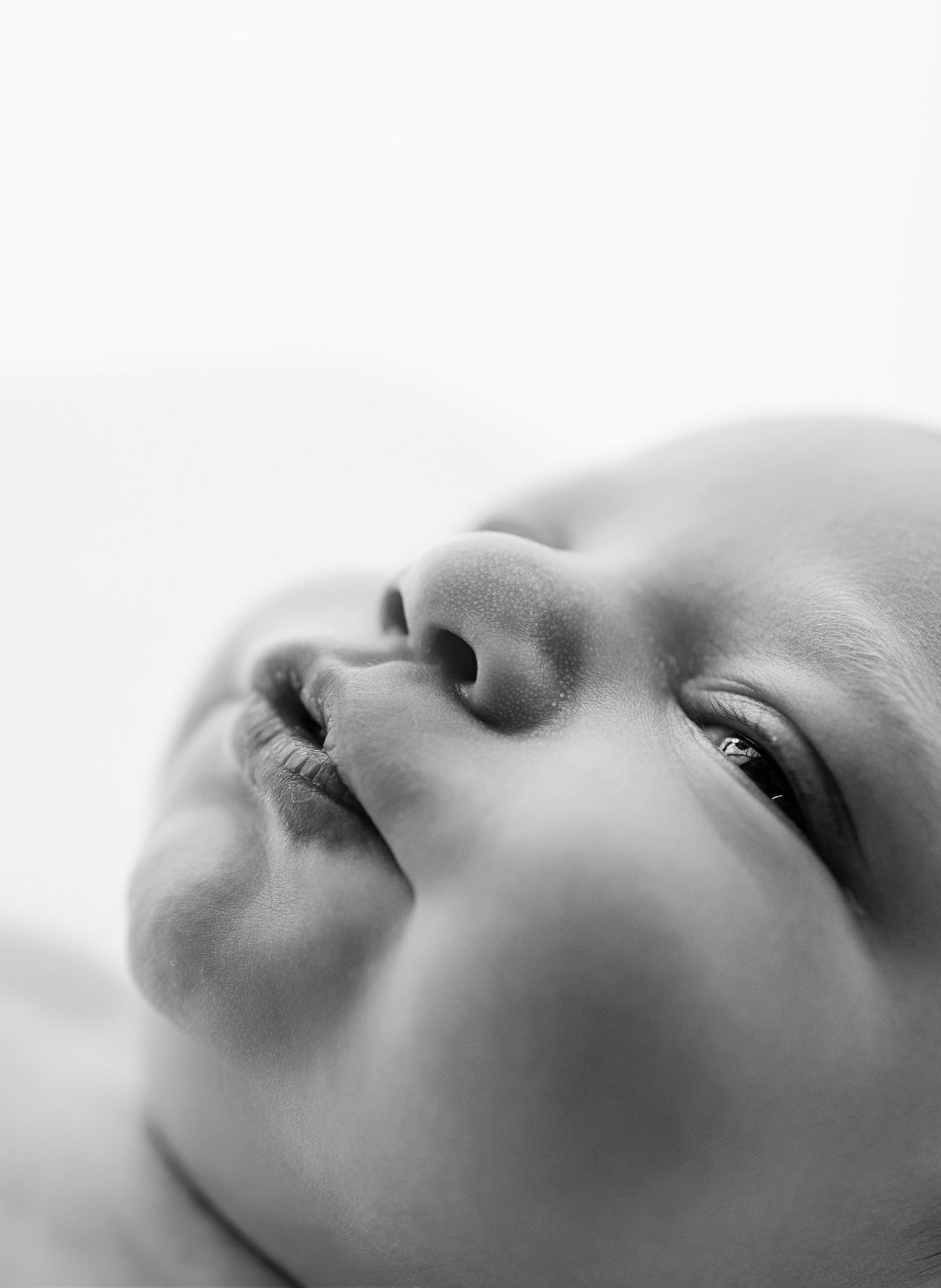 Close-up black and white portrait of a peaceful newborn baby looking upward, showcasing delicate facial features.