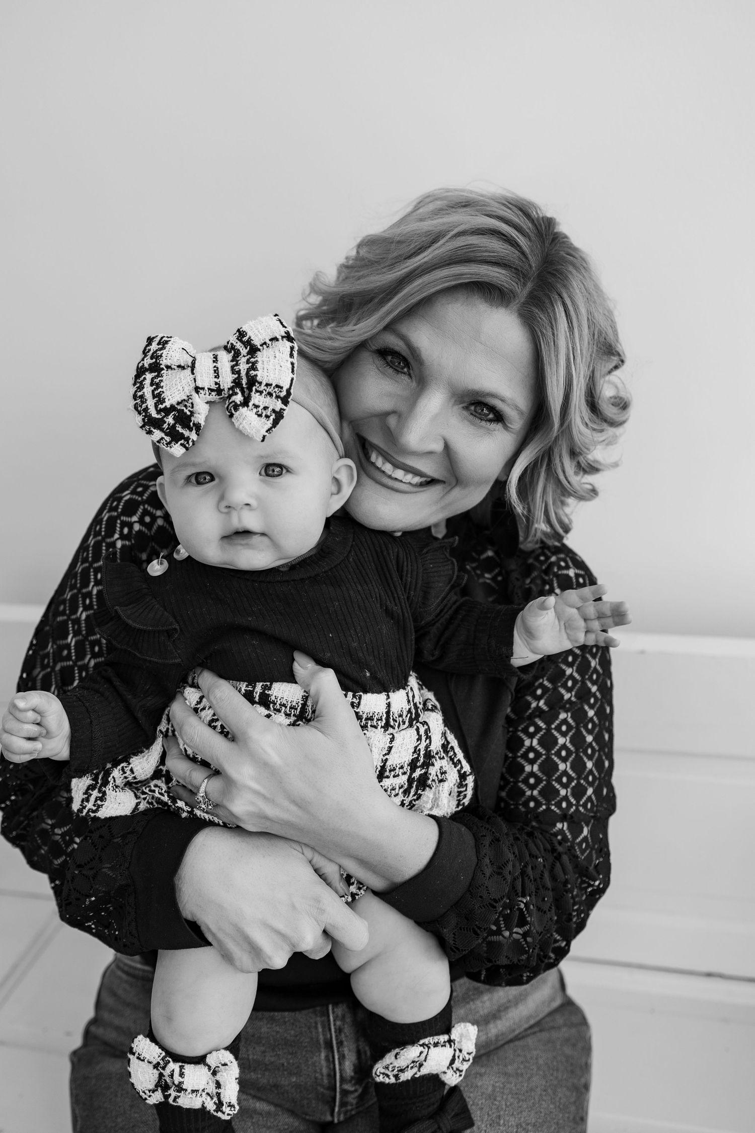 Black and white portrait of a smiling woman holding an adorable baby girl wearing a bow headband and matching outfit.
