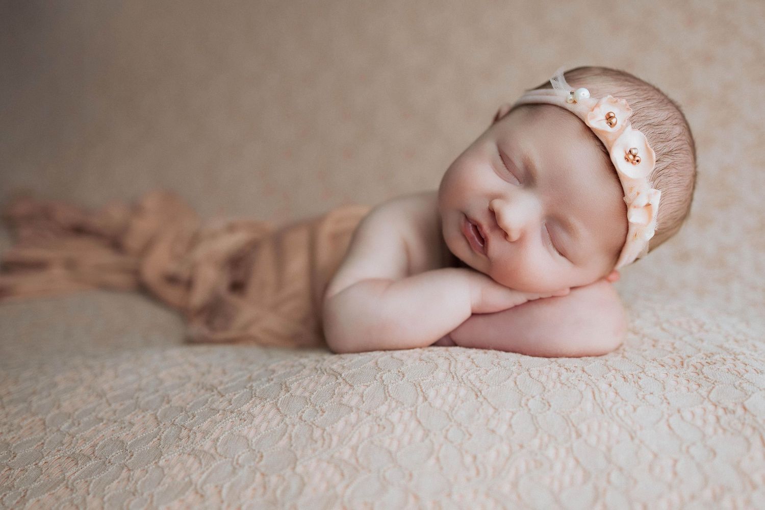 A serene sleeping newborn baby is curled up on soft beige fabric in a peaceful pose during a professional photo session.