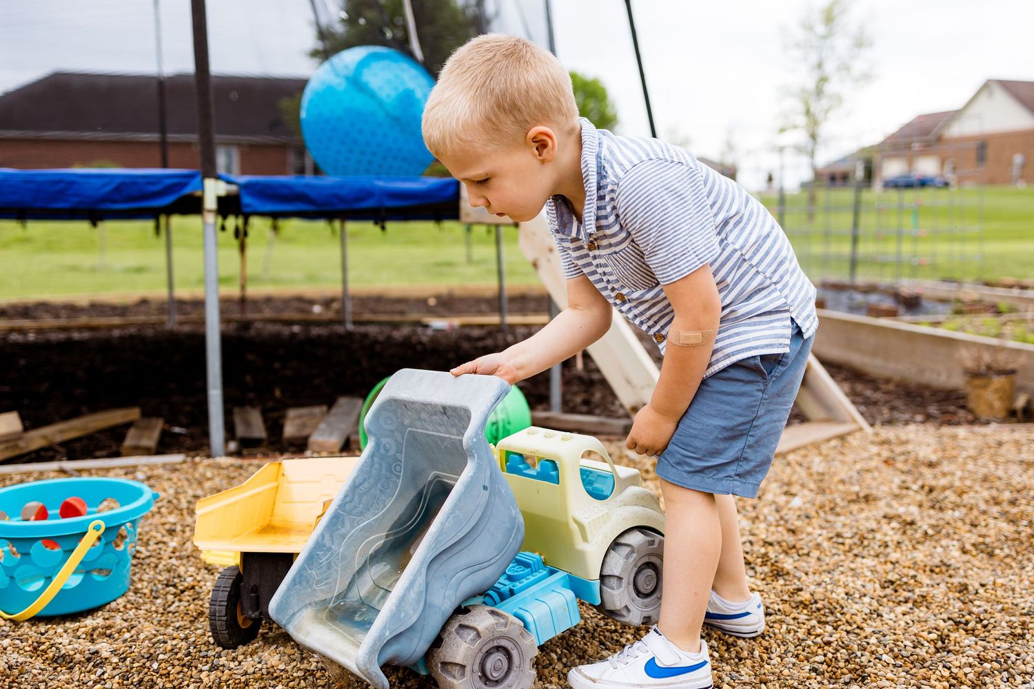 Child playing with a blue and gray toy dump truck in a backyard playground with mulch.