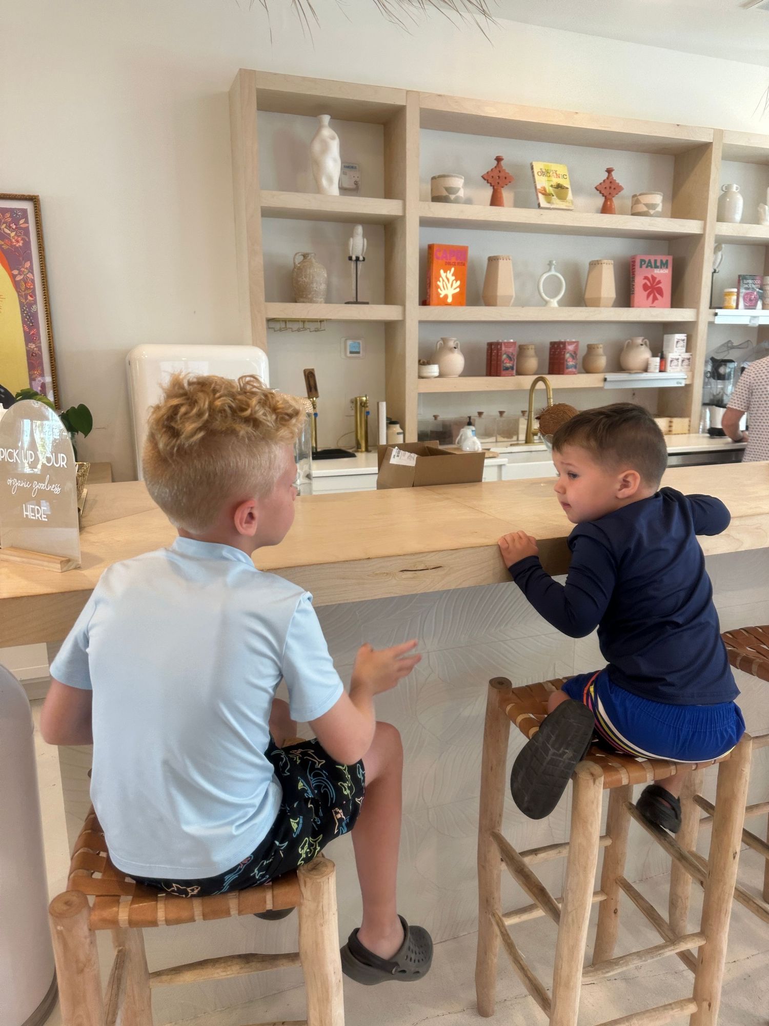 Two children sitting at counter with decorative shelving display in background.