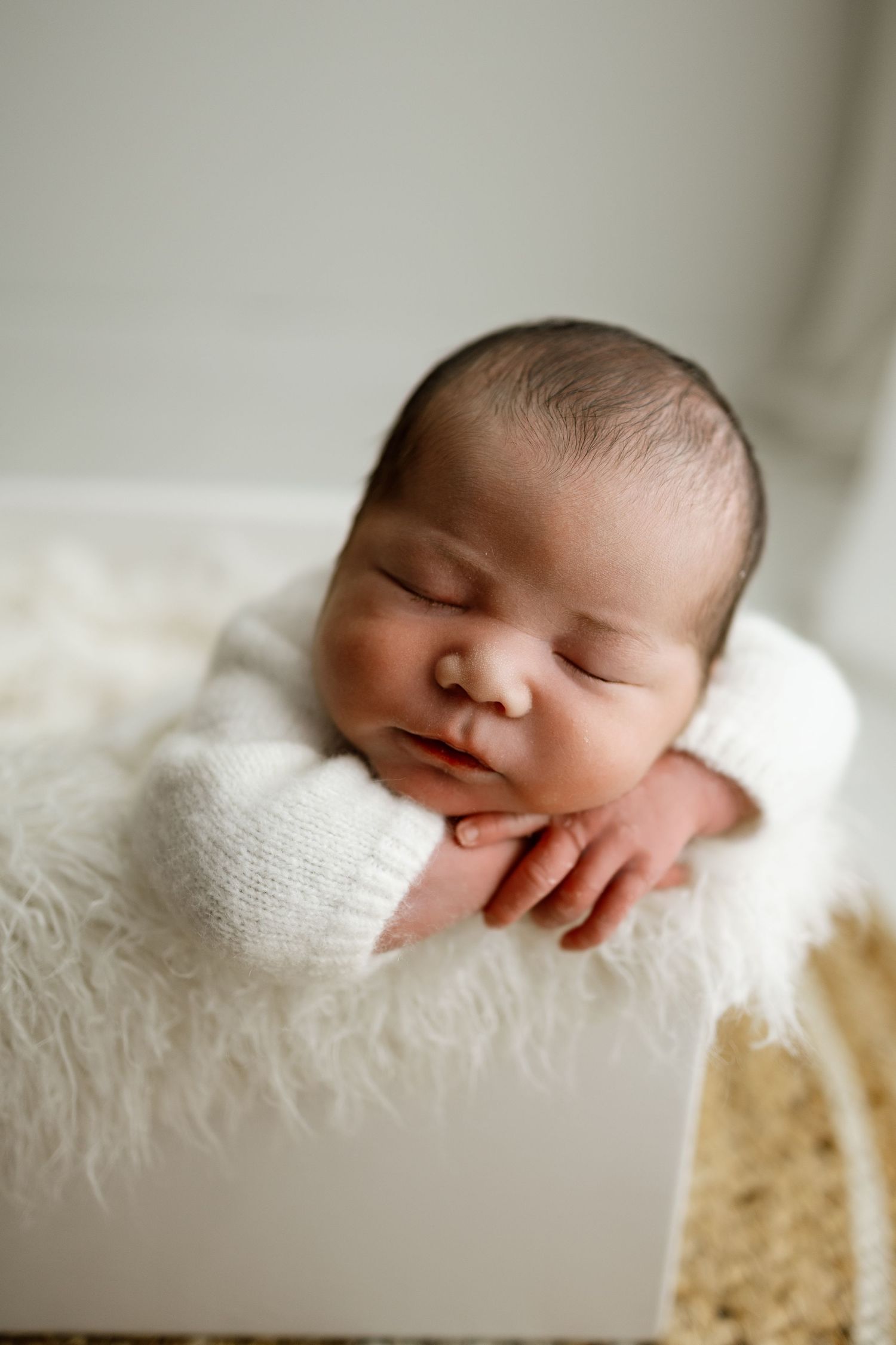Peaceful newborn baby sleeping on soft white blanket in natural light.
