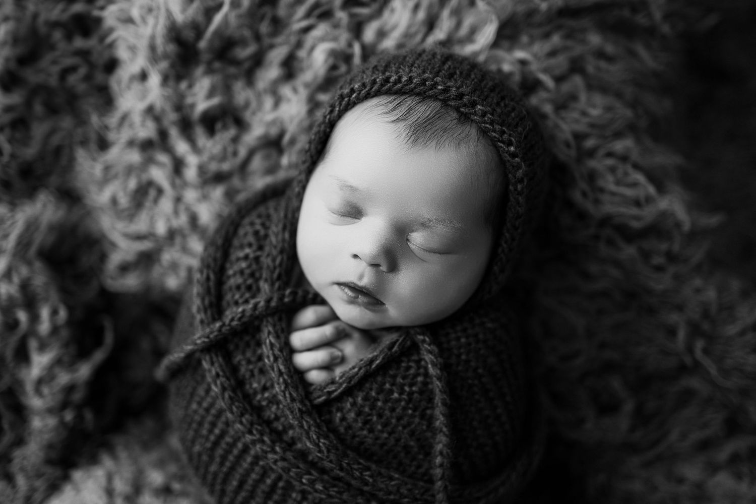 Baby wearing knit hat rests peacefully during newborn photo session in black and white.