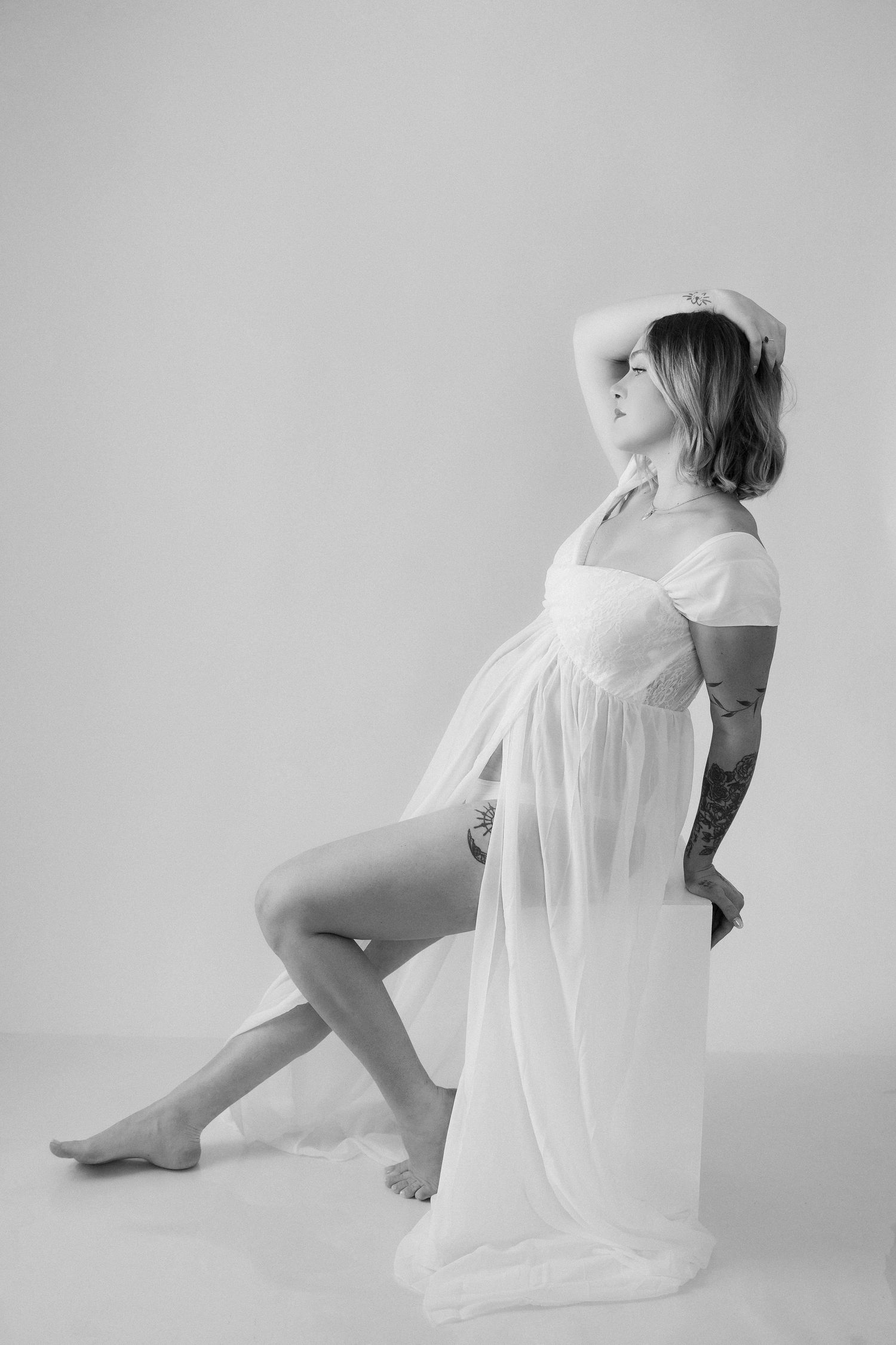 Artistic black and white maternity portrait of an expectant mother in flowing dress against grey backdrop.