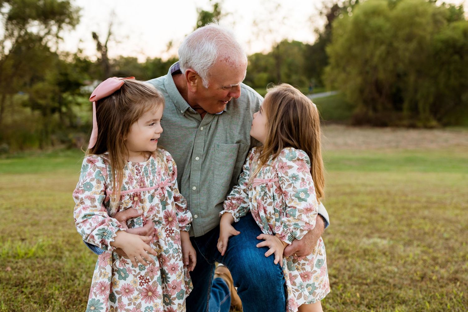 A loving moment shared between three generations in matching floral outfits on a grassy field at sunset.