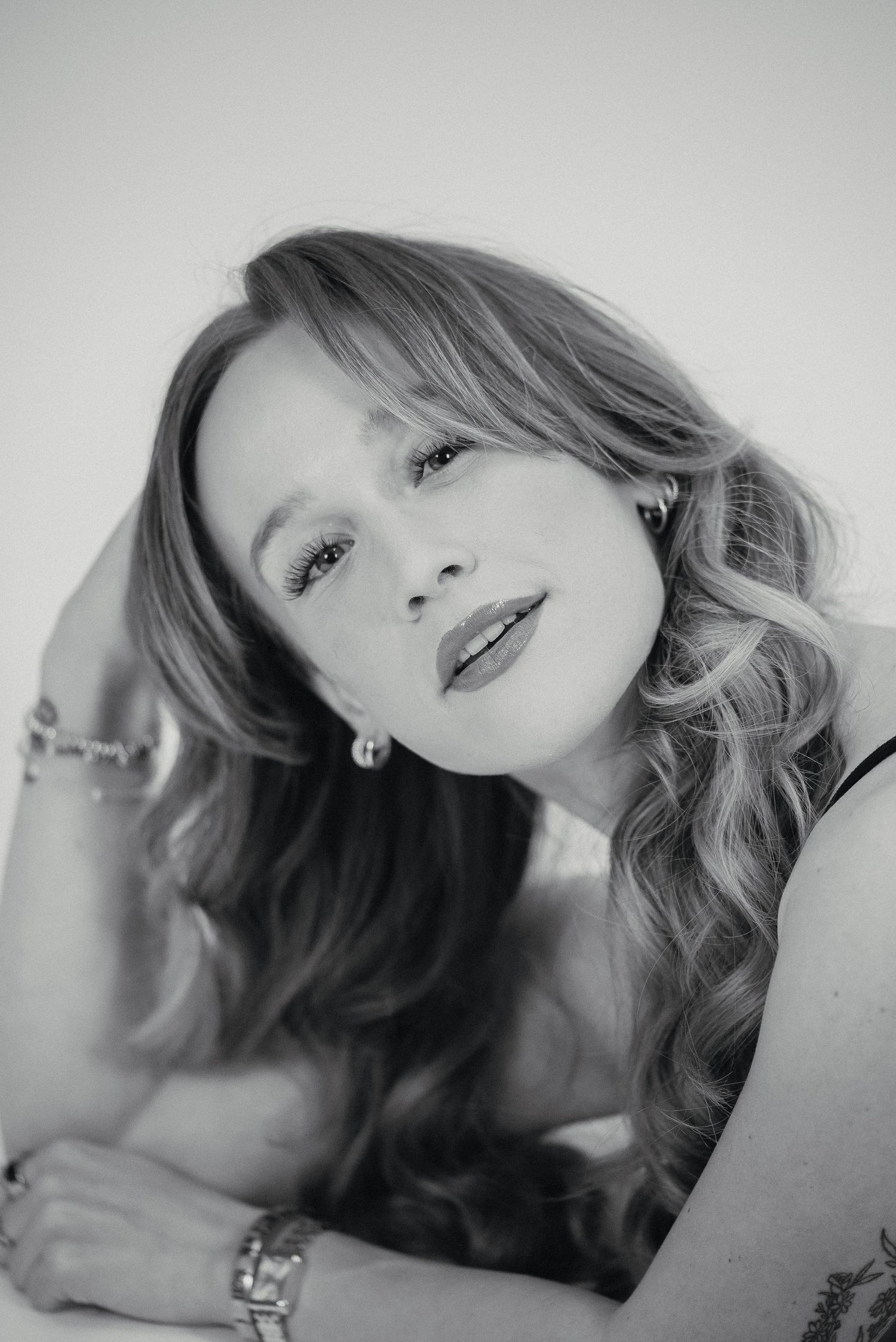 Black and white close-up portrait of a woman with wavy hair, pearl earrings, and a bracelet smiling softly.