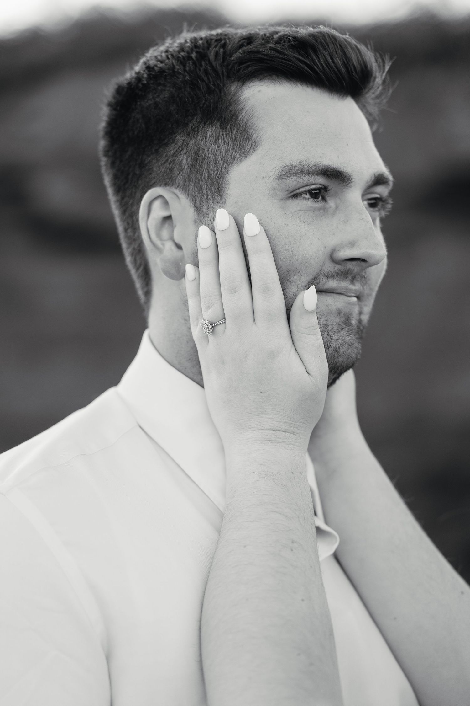 Black and white close-up of smiling groom with brides hand gently touching his cheek.