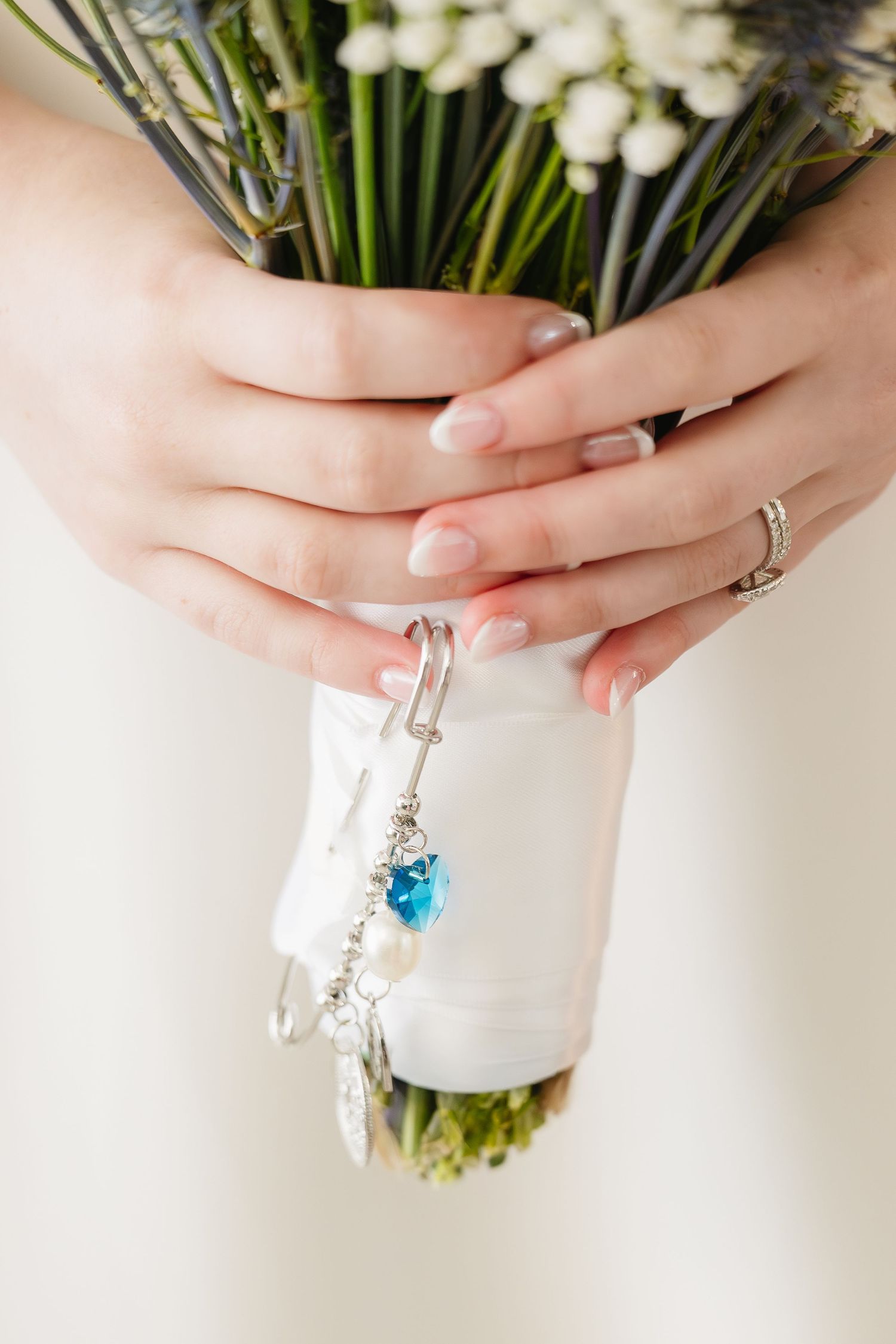 Close-up of bride holding bouquet with blue crystal heart charm and french manicured nails.