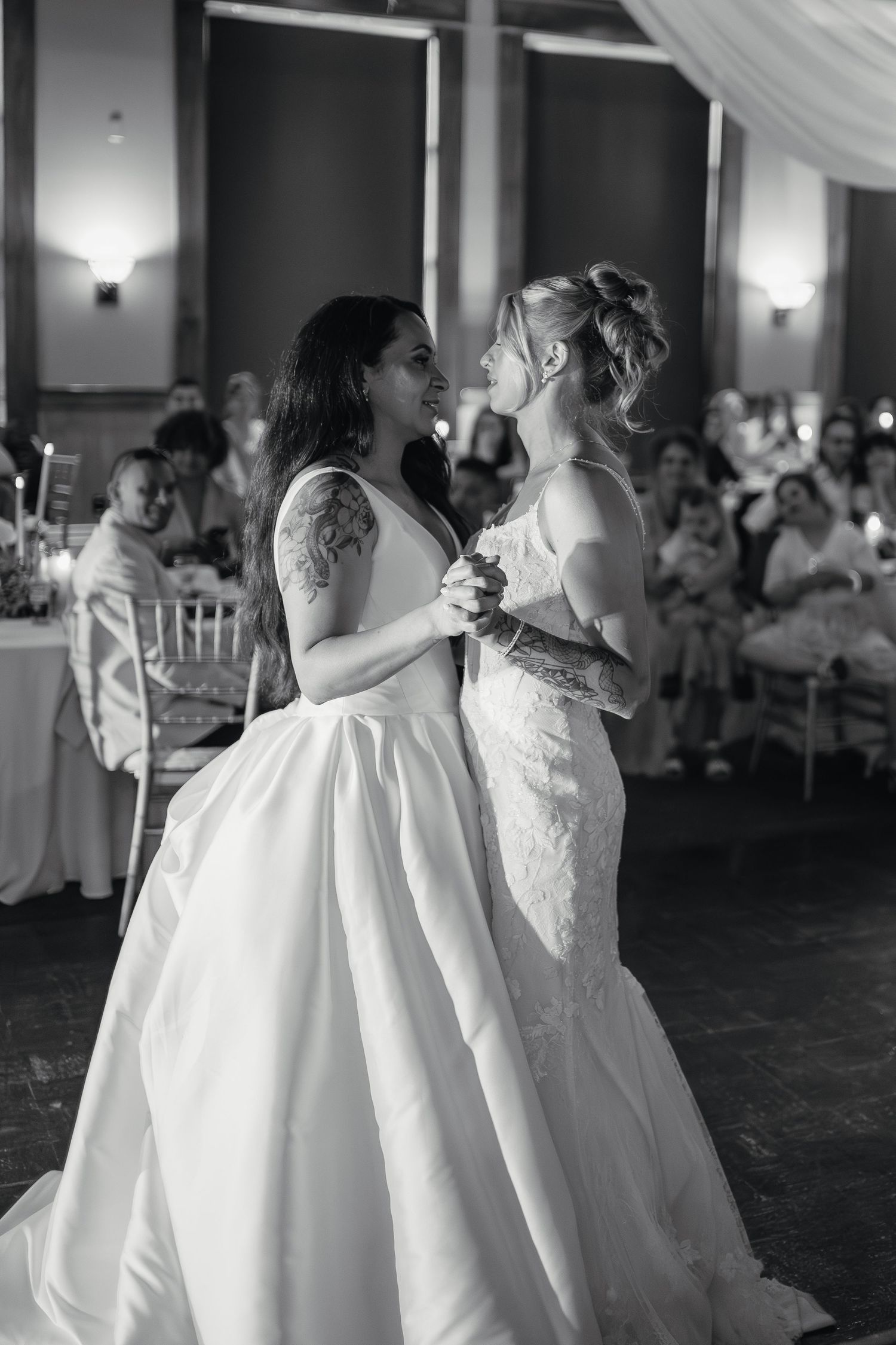 Black and white photo of two brides sharing their first dance together at their elegant wedding reception.