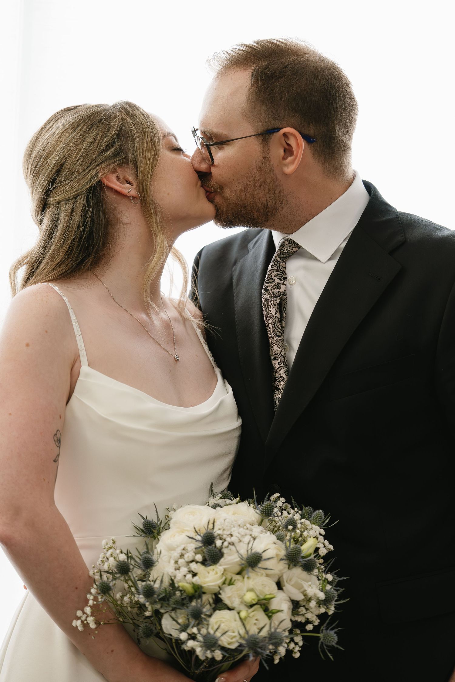 Bride and groom sharing romantic kiss while holding white and blue thistle wedding bouquet.