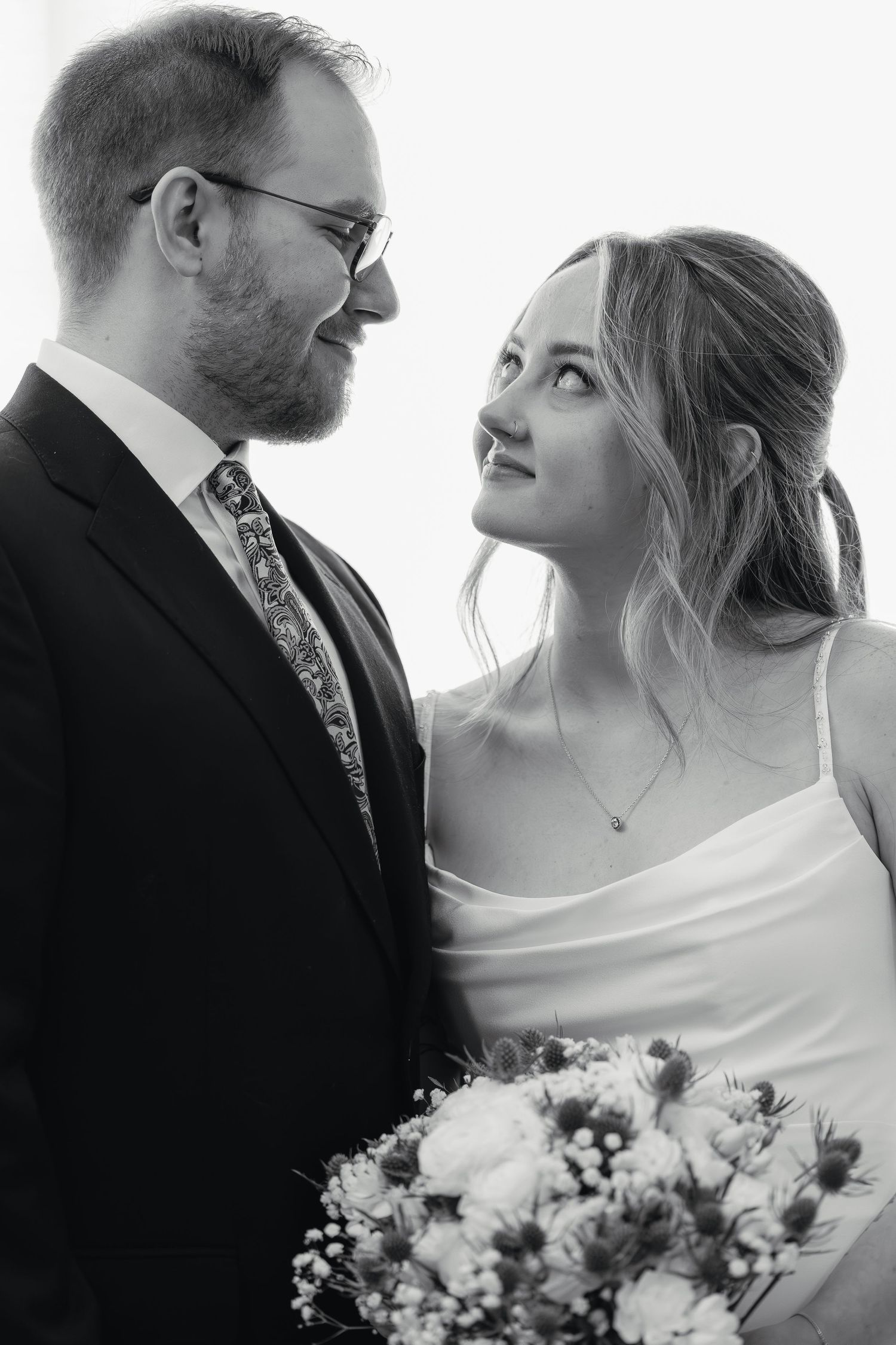 Black and white portrait of smiling bride and groom in suit and wedding dress holding floral bouquet.