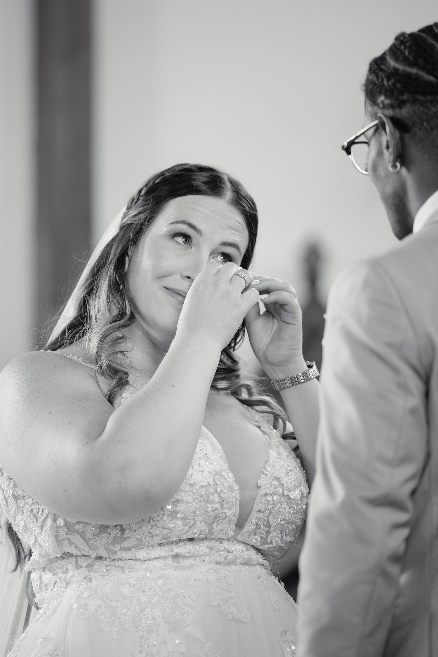 Emotional bride in lace gown wipes tears during heartfelt wedding ceremony moment.