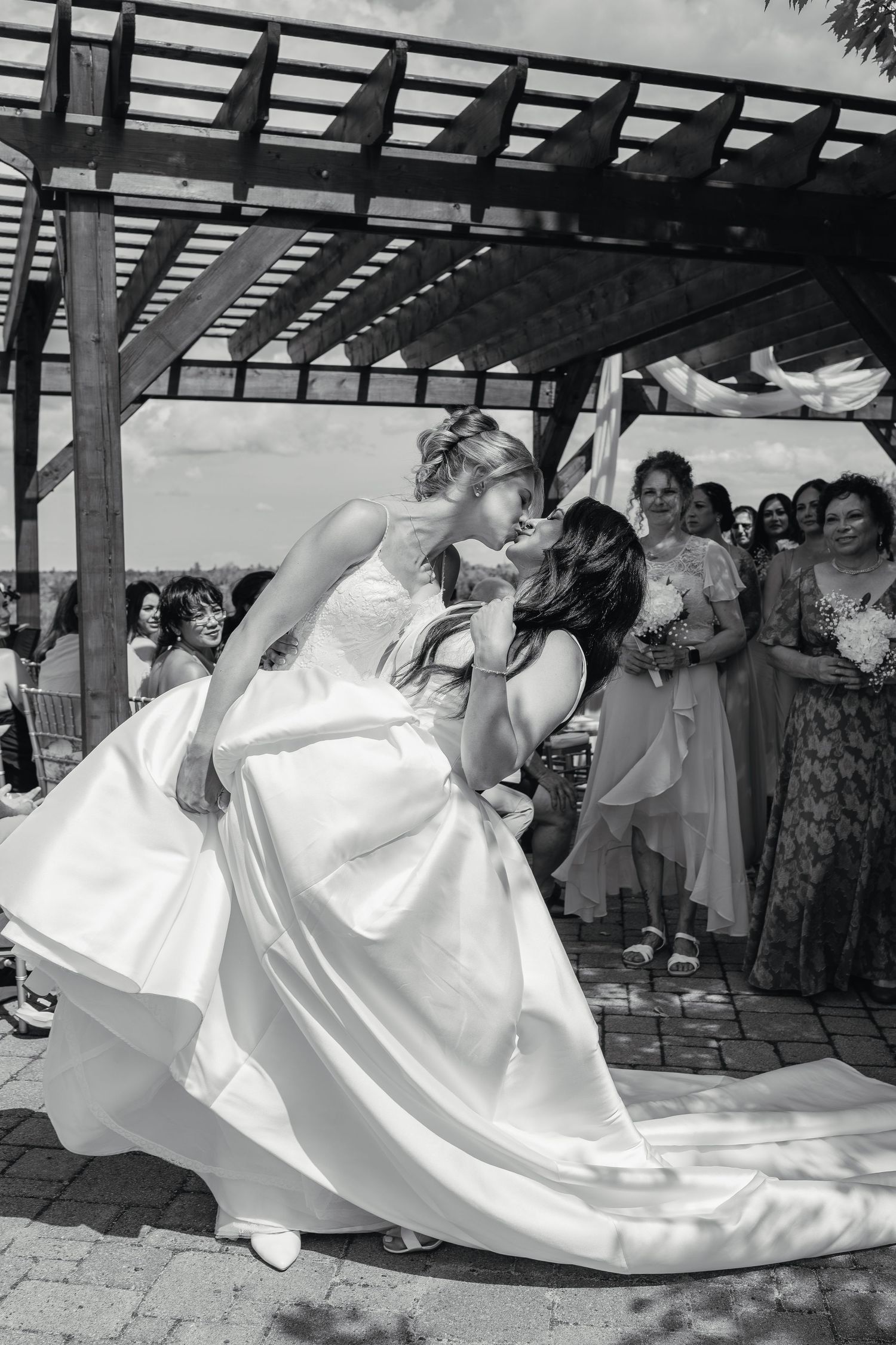 Black and white photo of two brides sharing a dramatic dip kiss at their outdoor wedding ceremony.