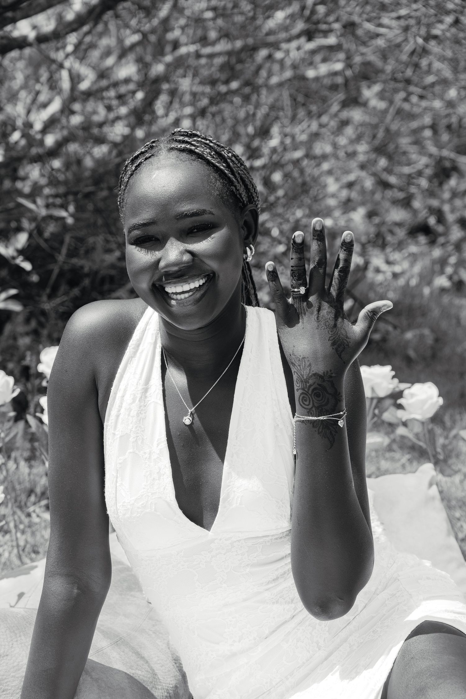 Black and white portrait of a smiling woman in white dress showing her engagement ring to the camera.