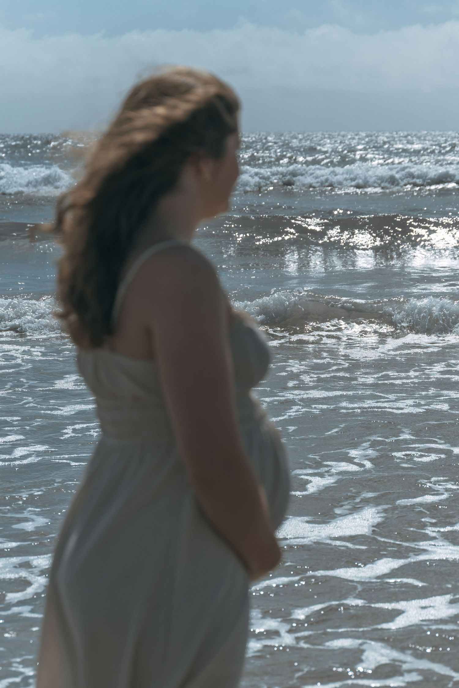 Pregnant mother standing on the beach with ocean in the background
