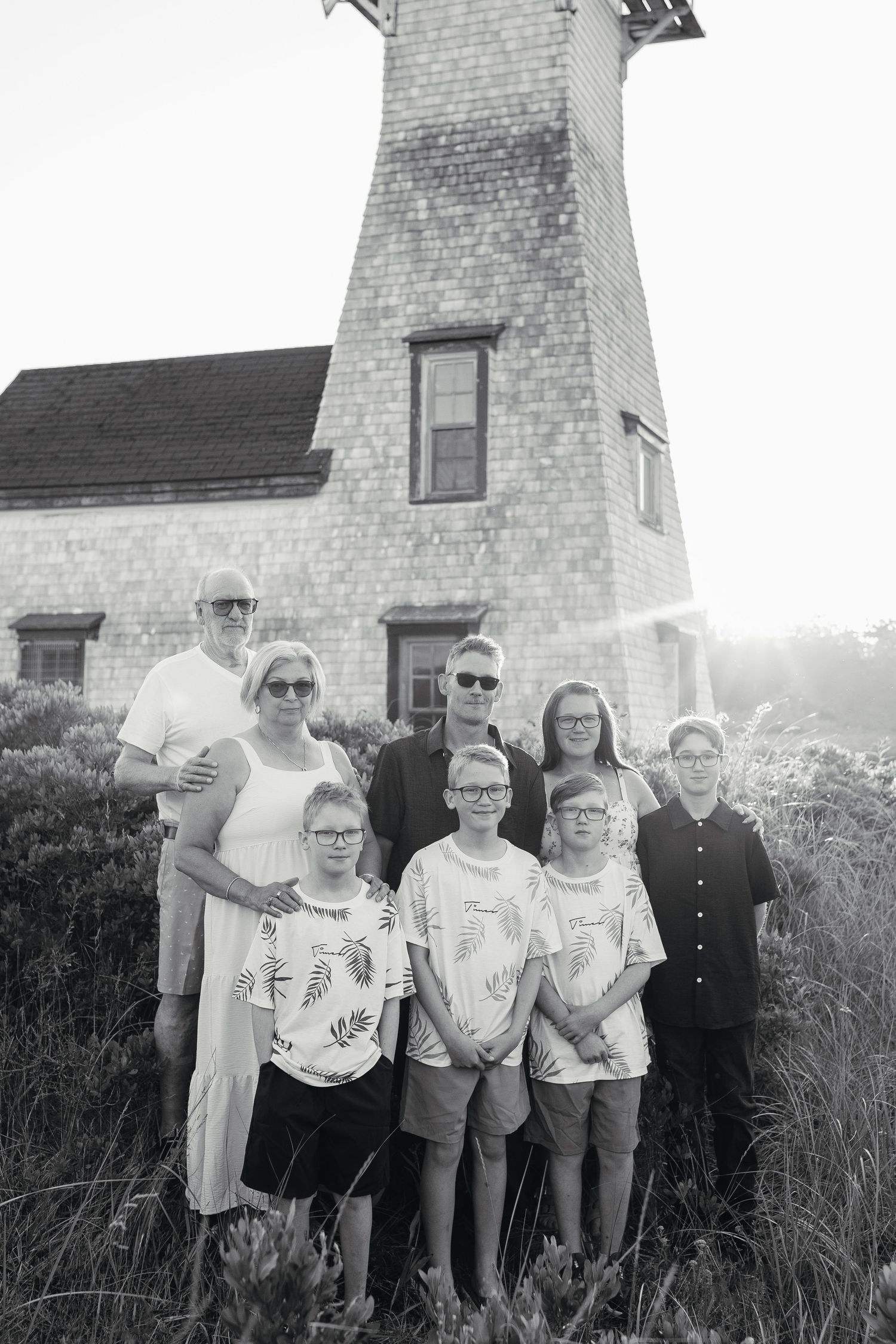 Black and white family photo of seven people posing in front of a historic lighthouse on a sunny day.
