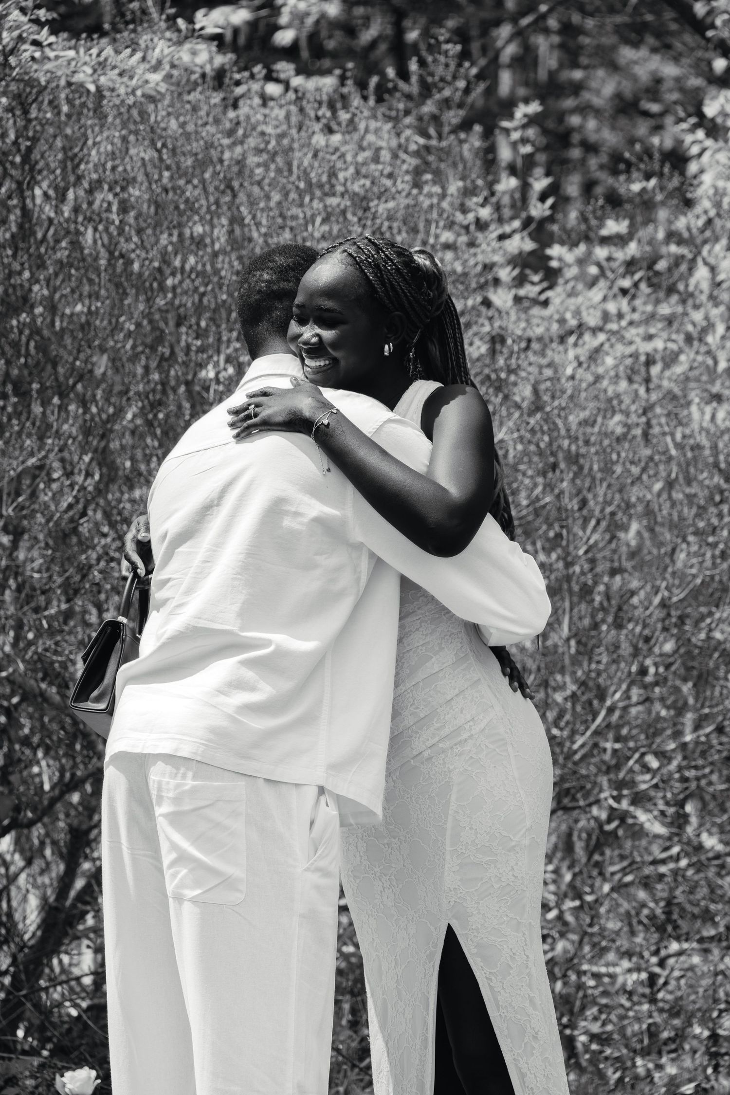 Black and white photo of a joyful couple embracing tightly outdoors after a marriage proposal.