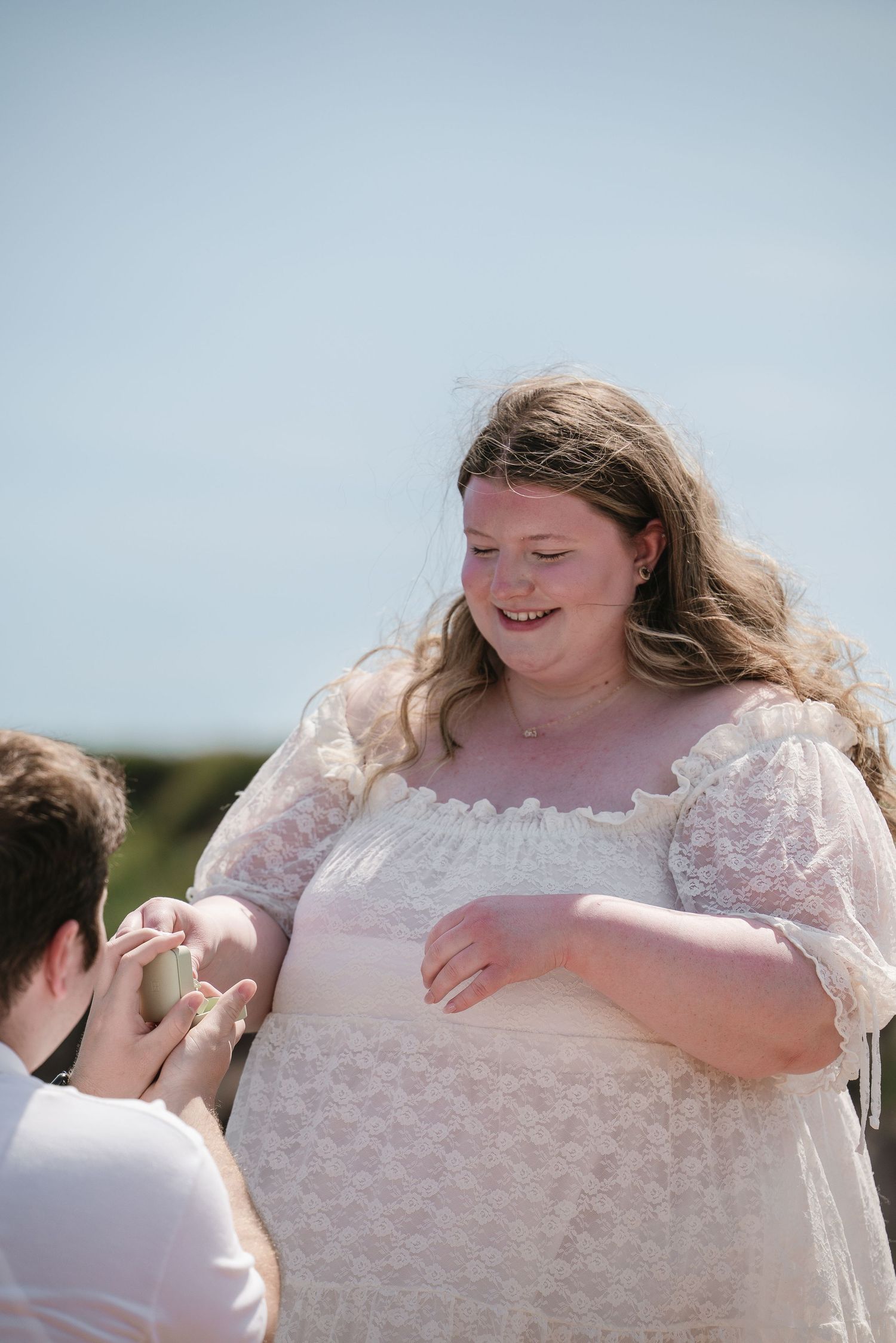 Joyful woman smiling as partner places engagement ring on her finger outdoors.