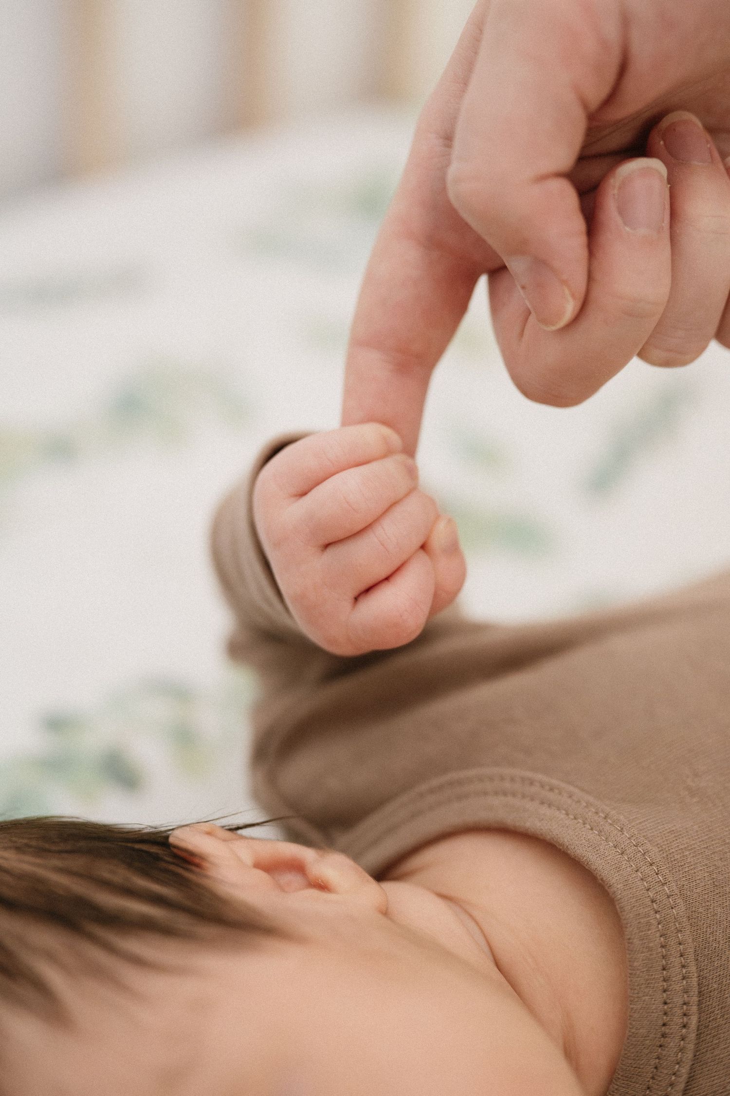 Tiny baby hands grabbing finger of parent during documentary-style newborn photography session.