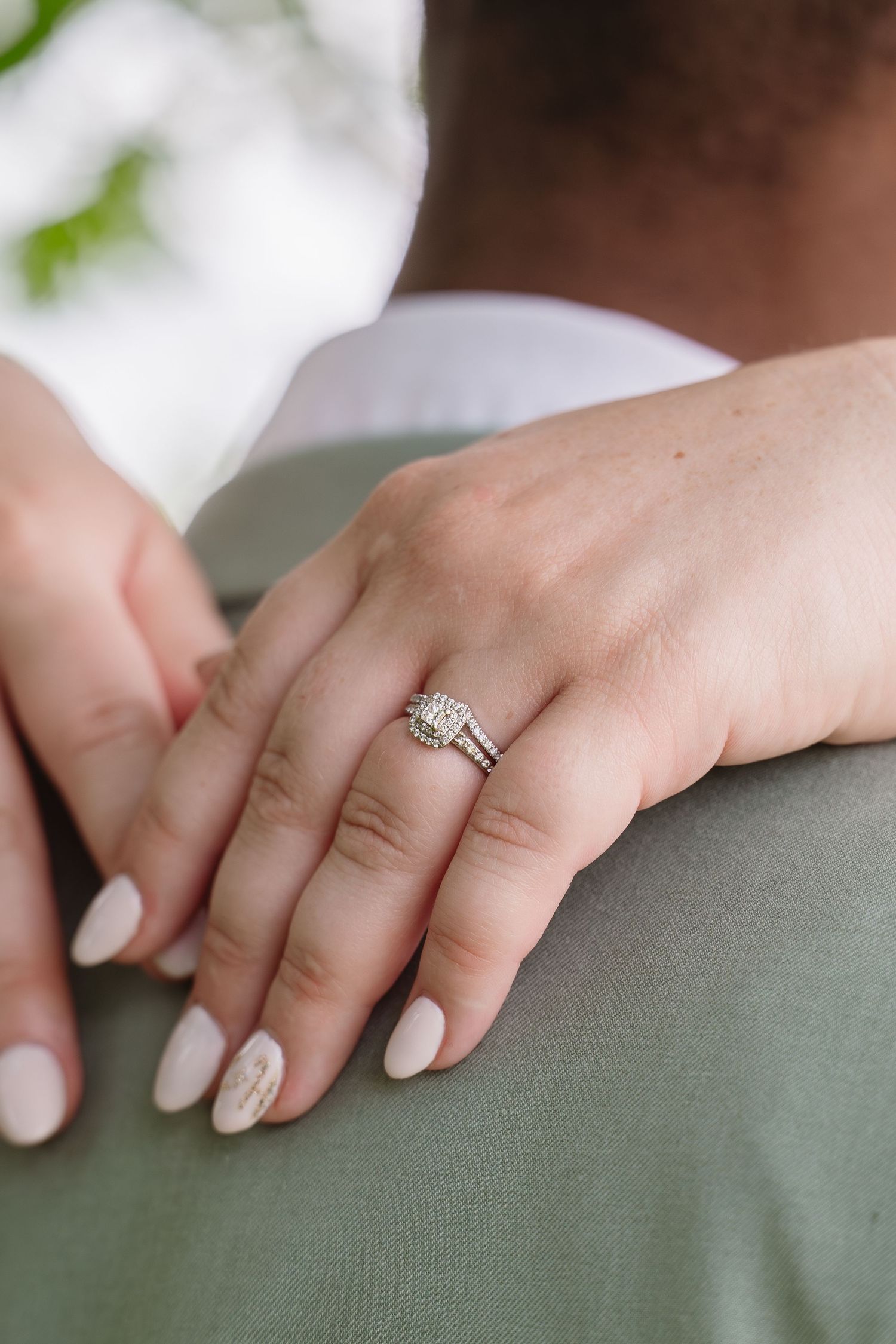 Close-up of bride's hand with diamond wedding ring set resting on groom's shoulder in sage suit.