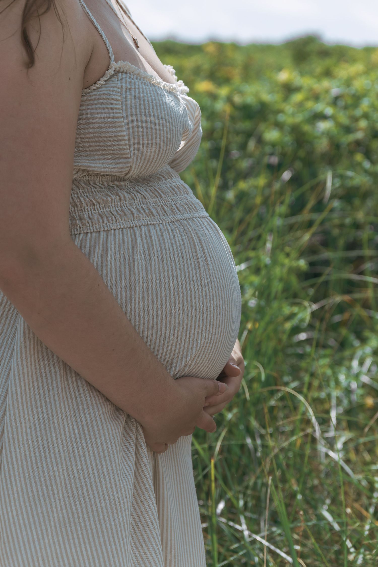 Expectant mother holding her baby bump during a beach maternity session in NS