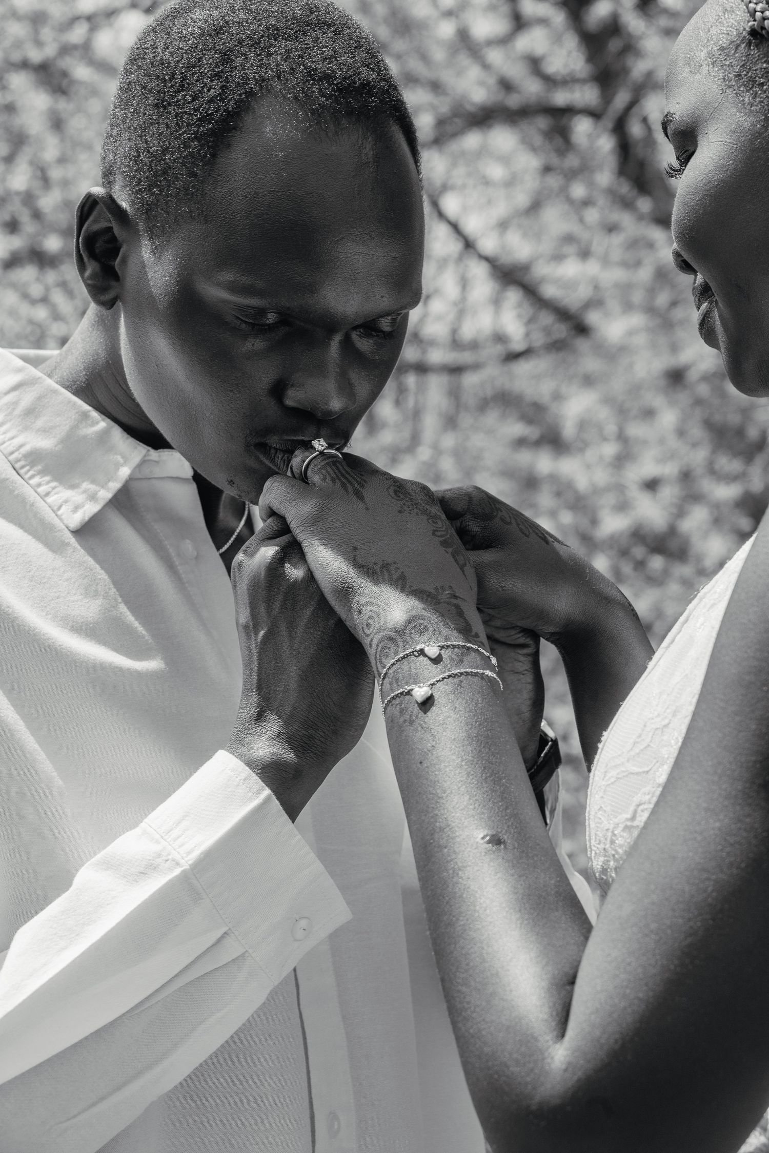 Black and white close-up of a man kissing his partners hand adorned with a bracelet and henna tattoo.
