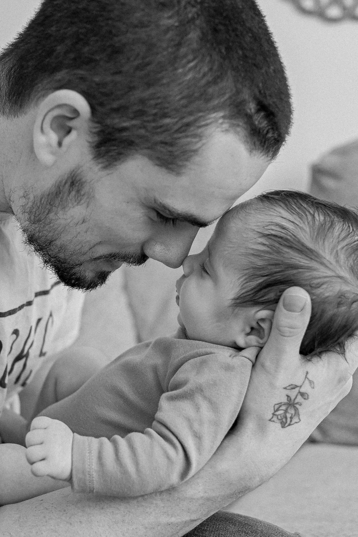 Black and white photo of a bearded father tenderly touching foreheads with his newborn baby.
