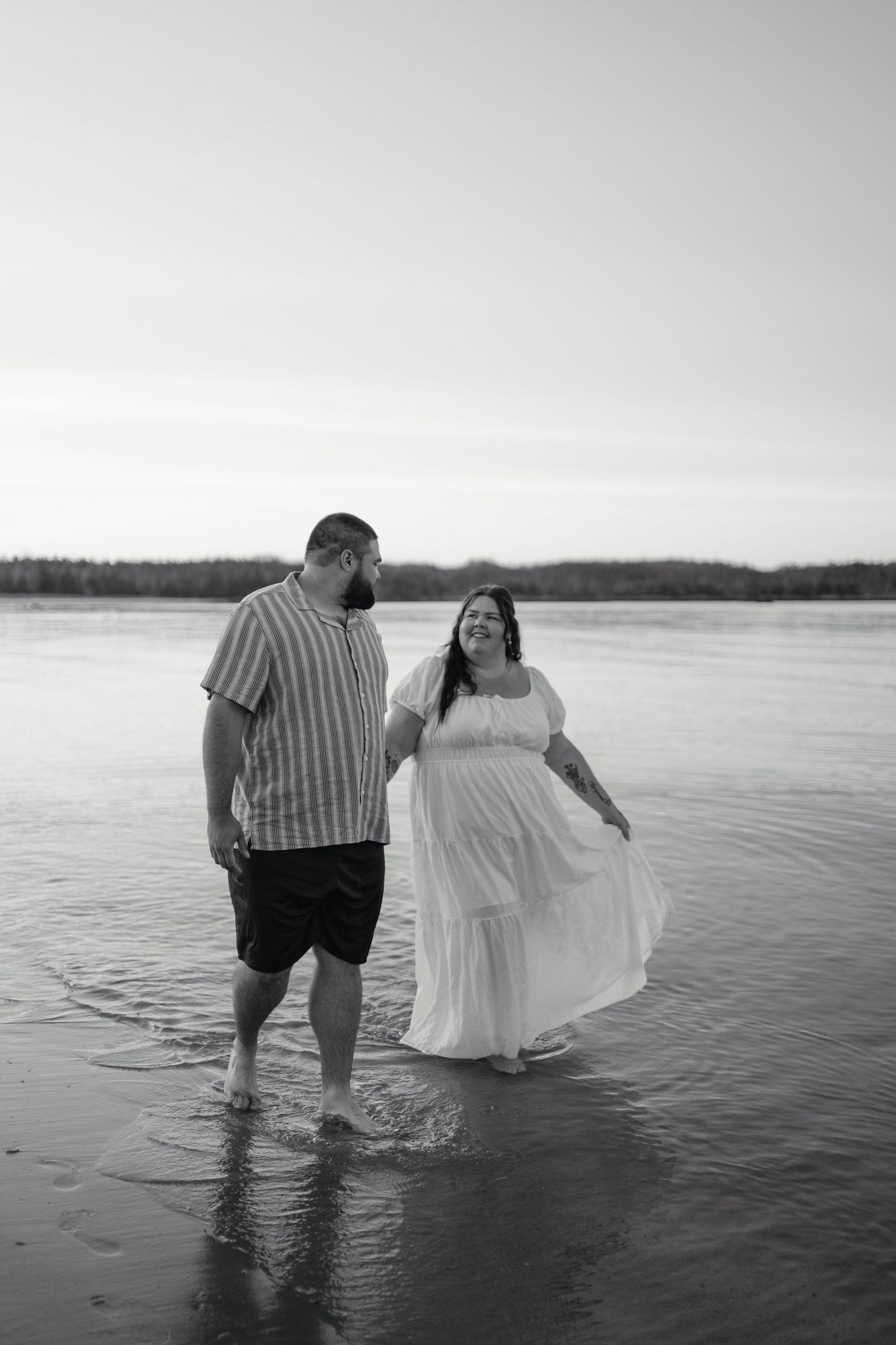 Couple walking hand in hand through shallow water at beach during golden hour sunset.