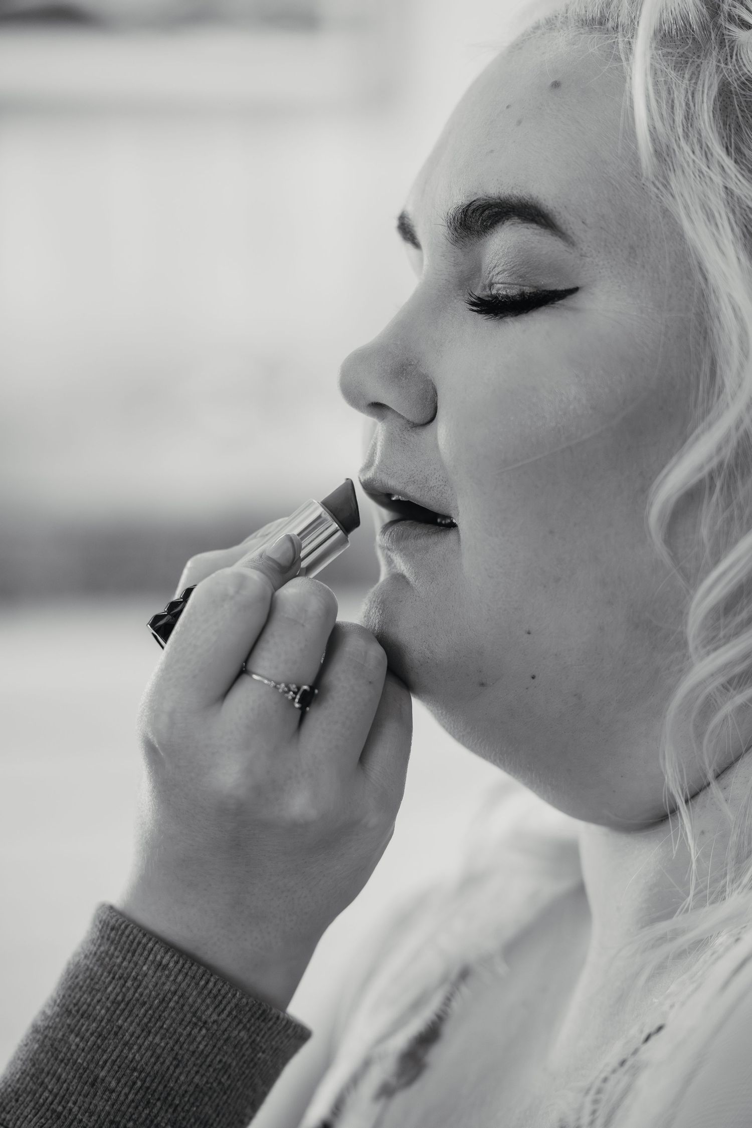 Black and white close-up of makeup artist applying lipstick to blonde bride before wedding.