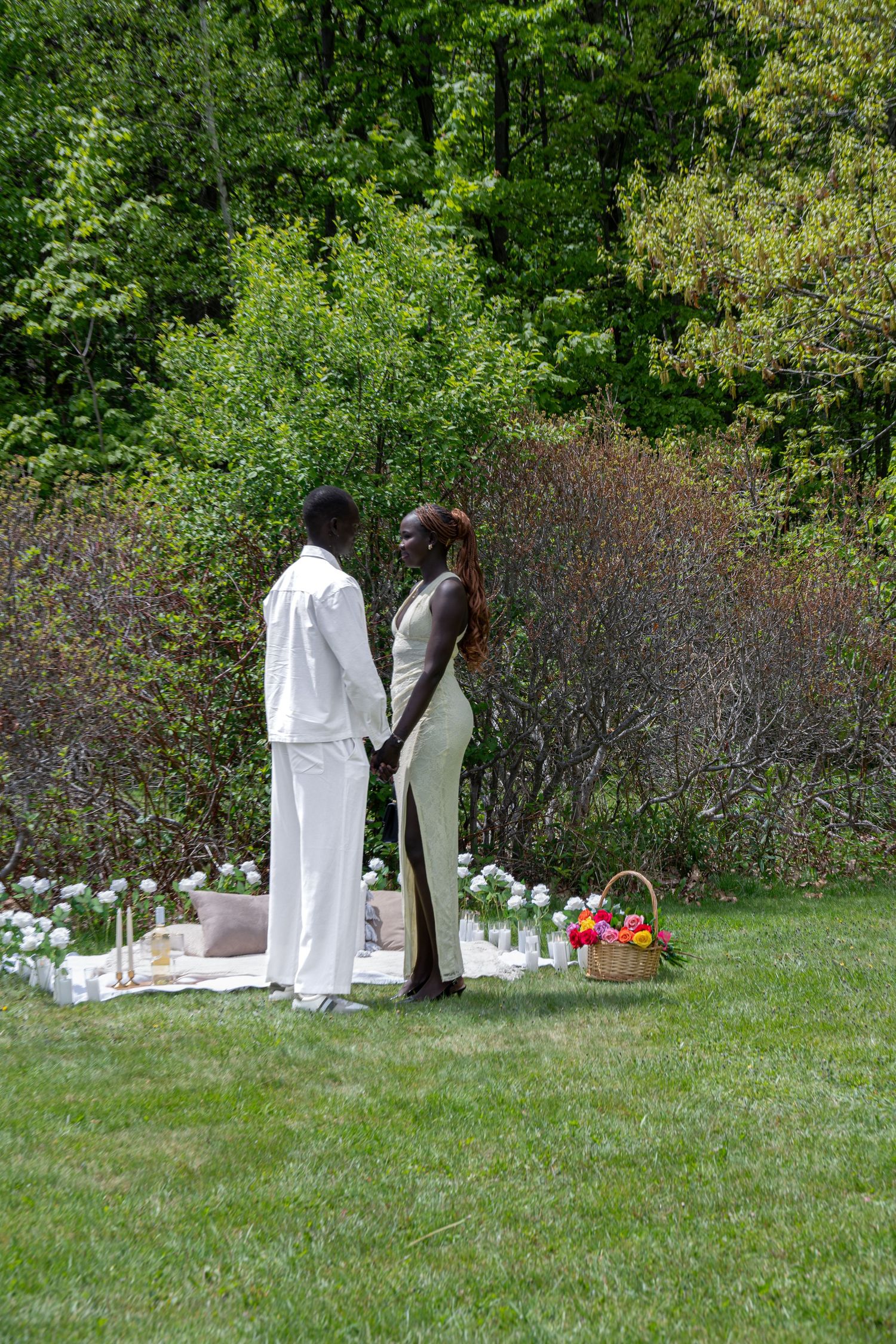 Couple holding hands facing each other at an elegant outdoor proposal setup with white floral decorations.