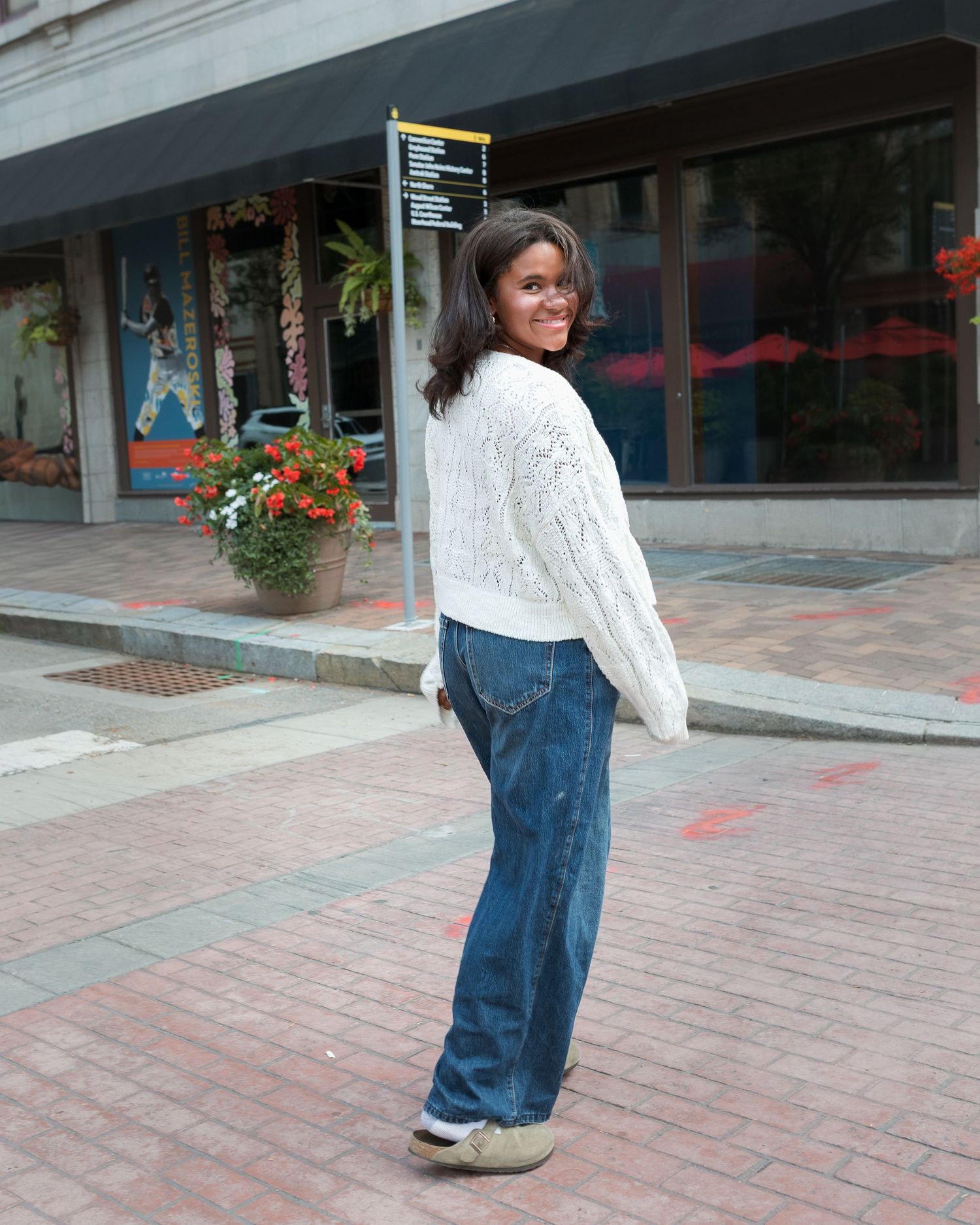 A person walks along a brick paved courtyard wearing jeans and a white sweater.