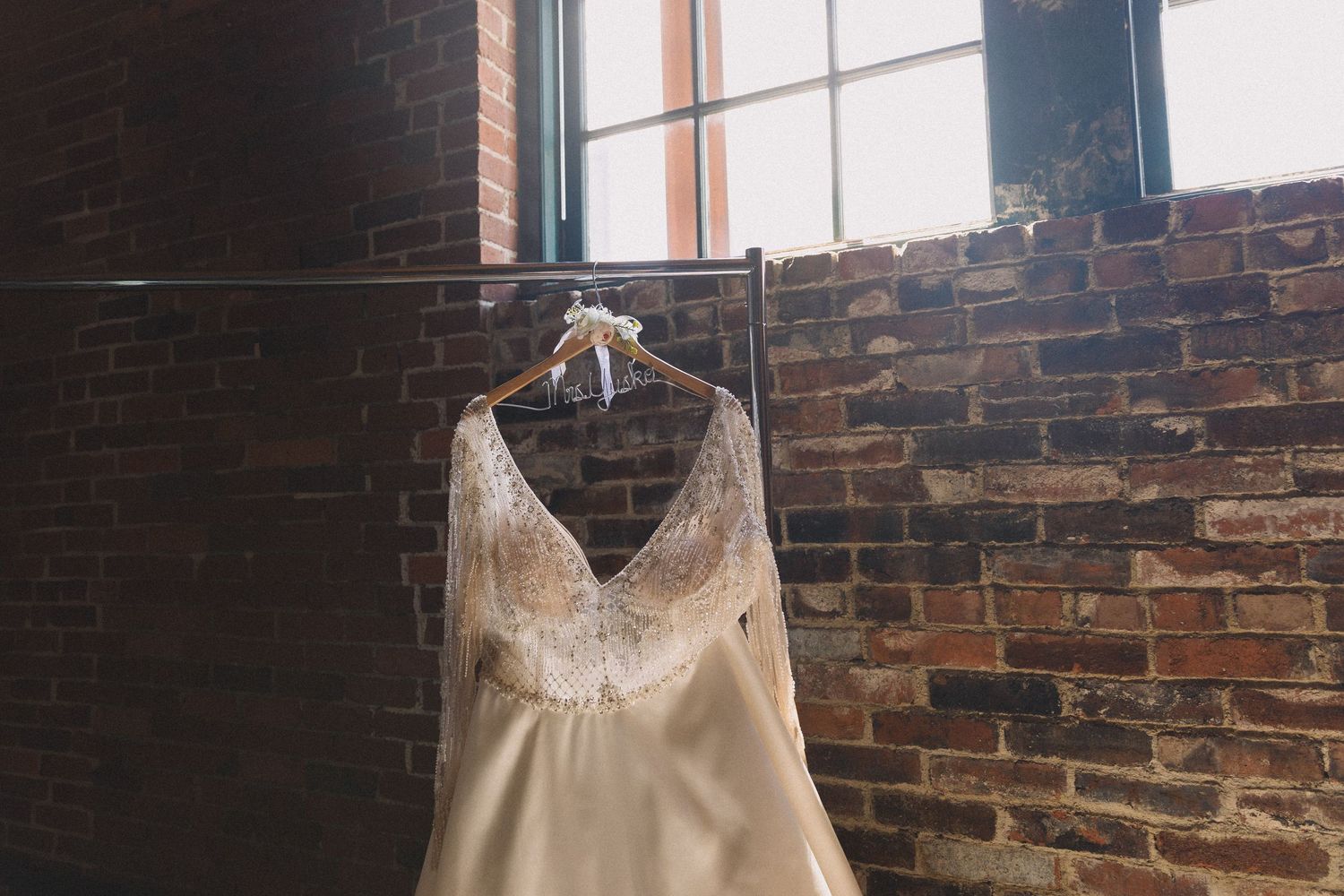 An elegant cream-colored wedding dress hanging against a rustic exposed brick wall.