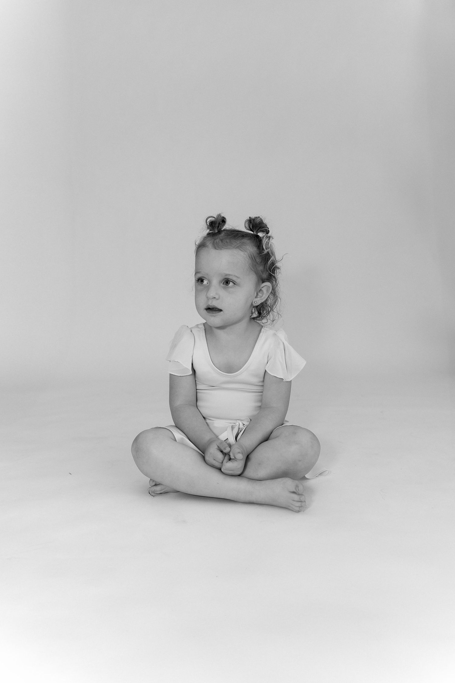 Black and white portrait of young child in ballet outfit sitting cross-legged.