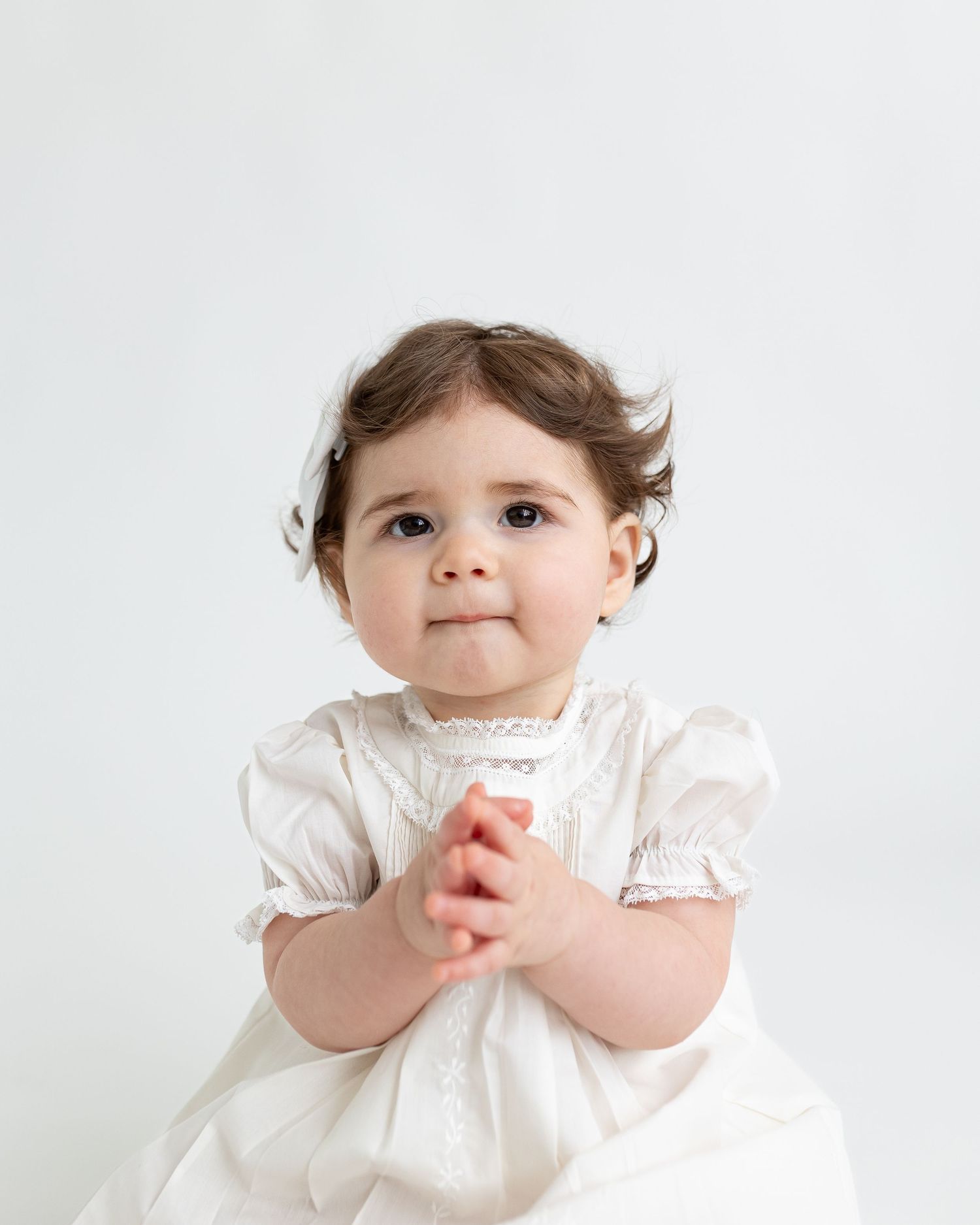 Baby in white dress sitting against white background in three similar poses.