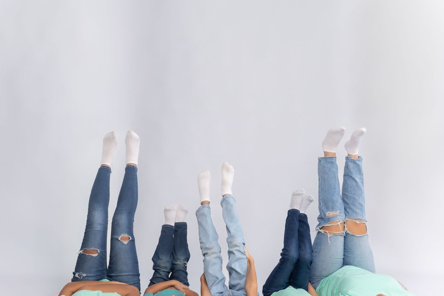 Playful sibling photo with legs up against a white backdrop, creative family portrait with cozy denim and neutral tones.