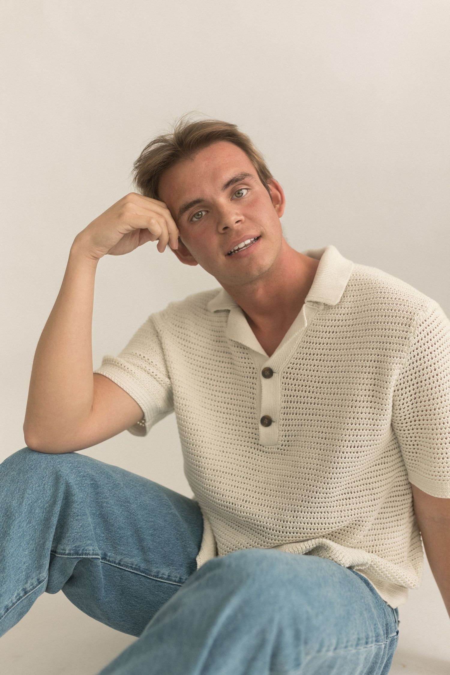 Portrait of person in cream knit polo shirt sitting casually against white studio backdrop.