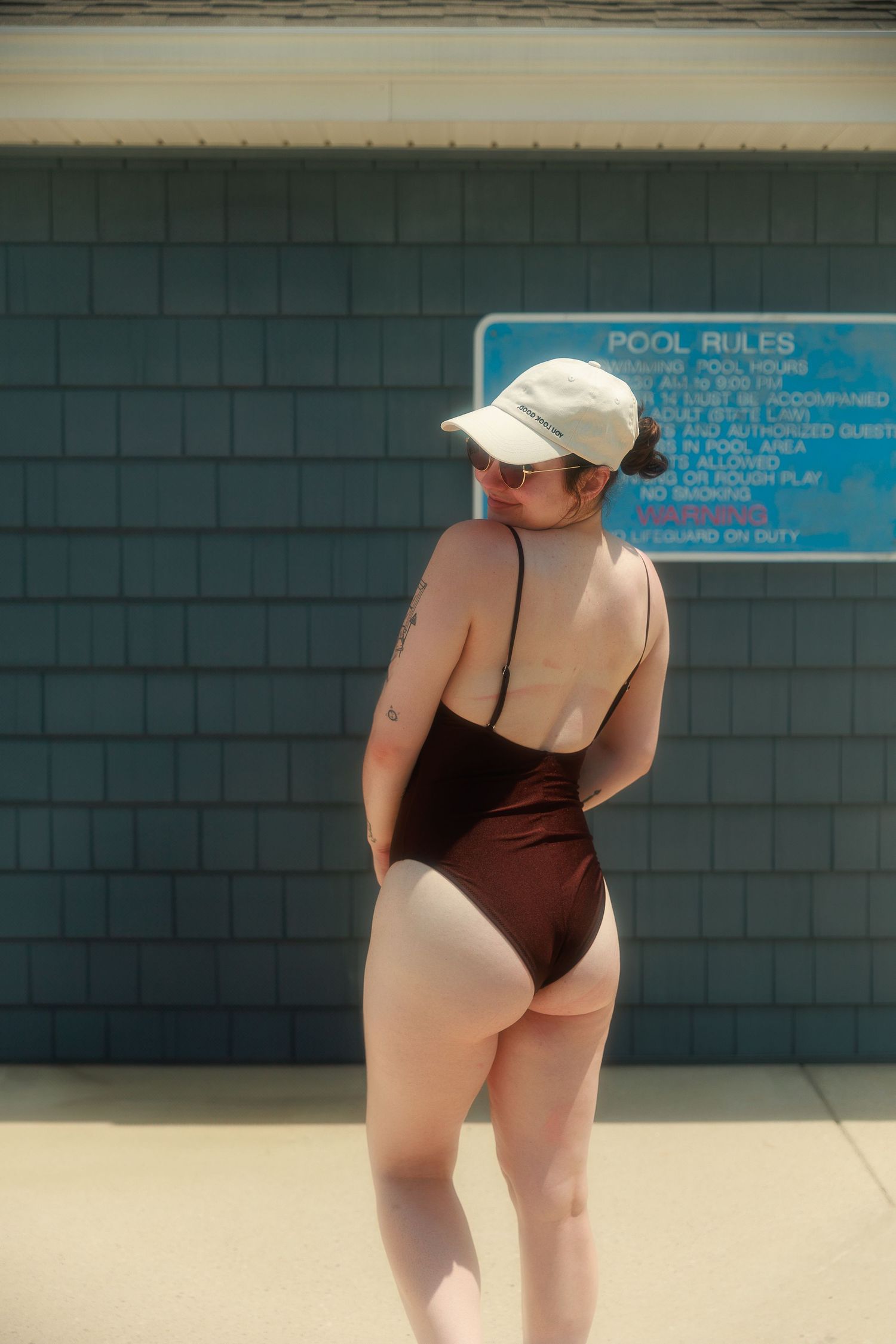 Person in brown swimsuit and baseball cap at poolside.