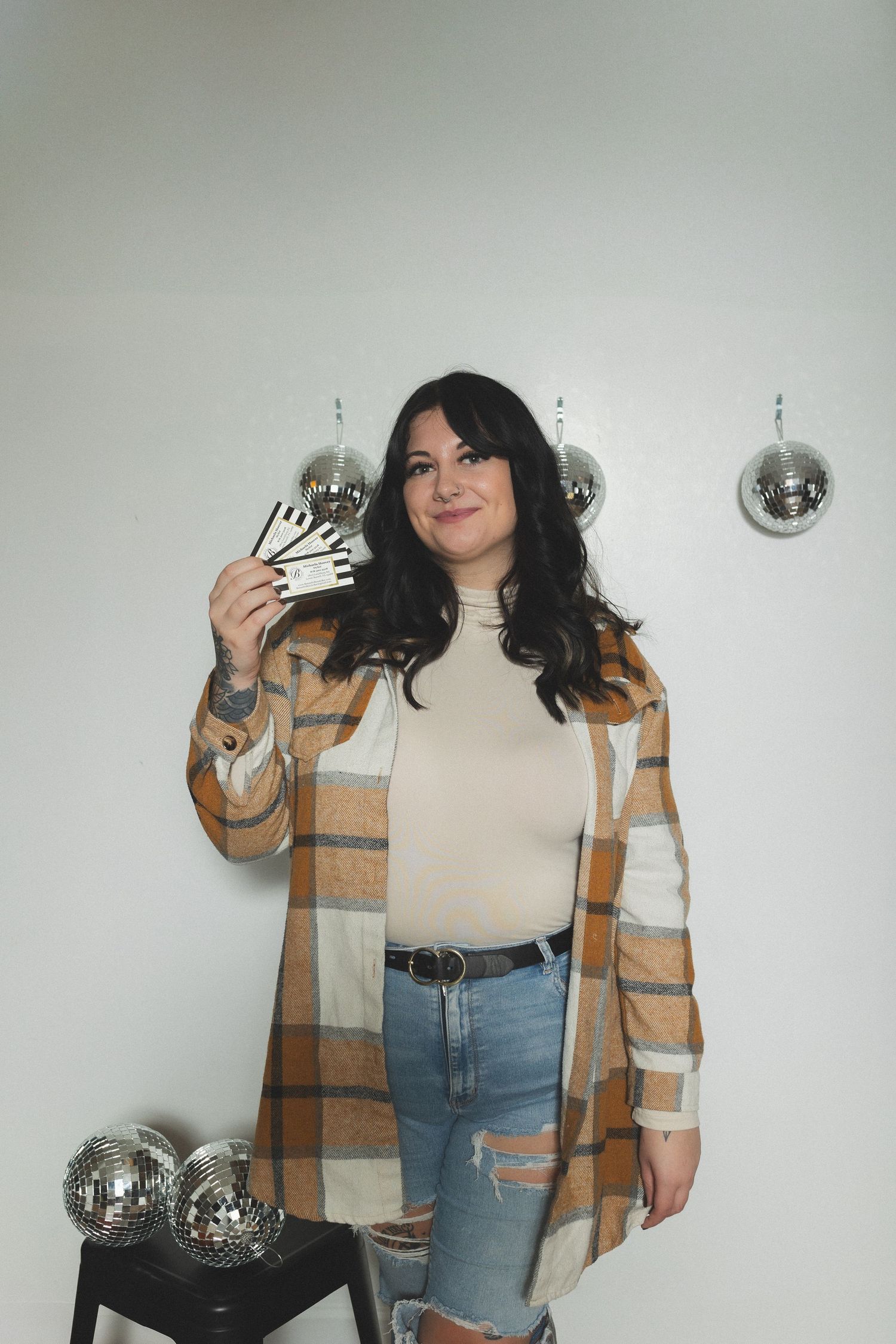 Person in striped cardigan posing with disco balls against white wall.